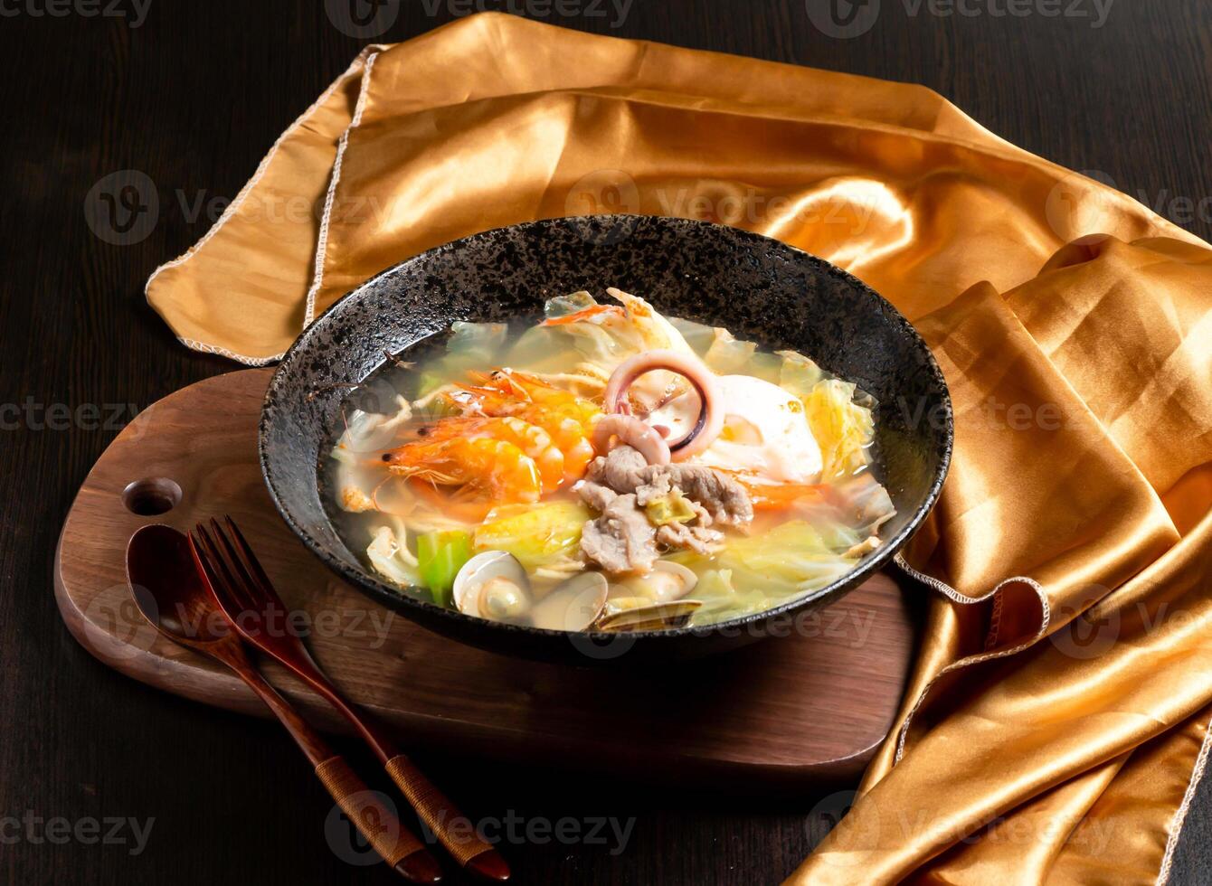 seafood and chicken pot roast with shrimp, squid rings, fork and spoon served in dish isolated on wooden board side view of asian food photo