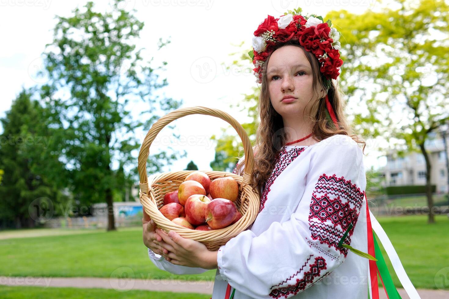 young beautiful girl in red wreath of flowers on her head red poppies in vyshyvanka red apples take an apple with hands inhale smell good weather in garden For world beautiful girls women of the world photo