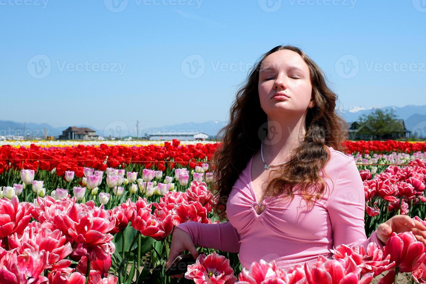 a beautiful young girl raised her face in the wind looks closed her eyes inhales fresh air stands in a field of tulips red tulips with a white border against clear blue sky freshness joy freedom will photo