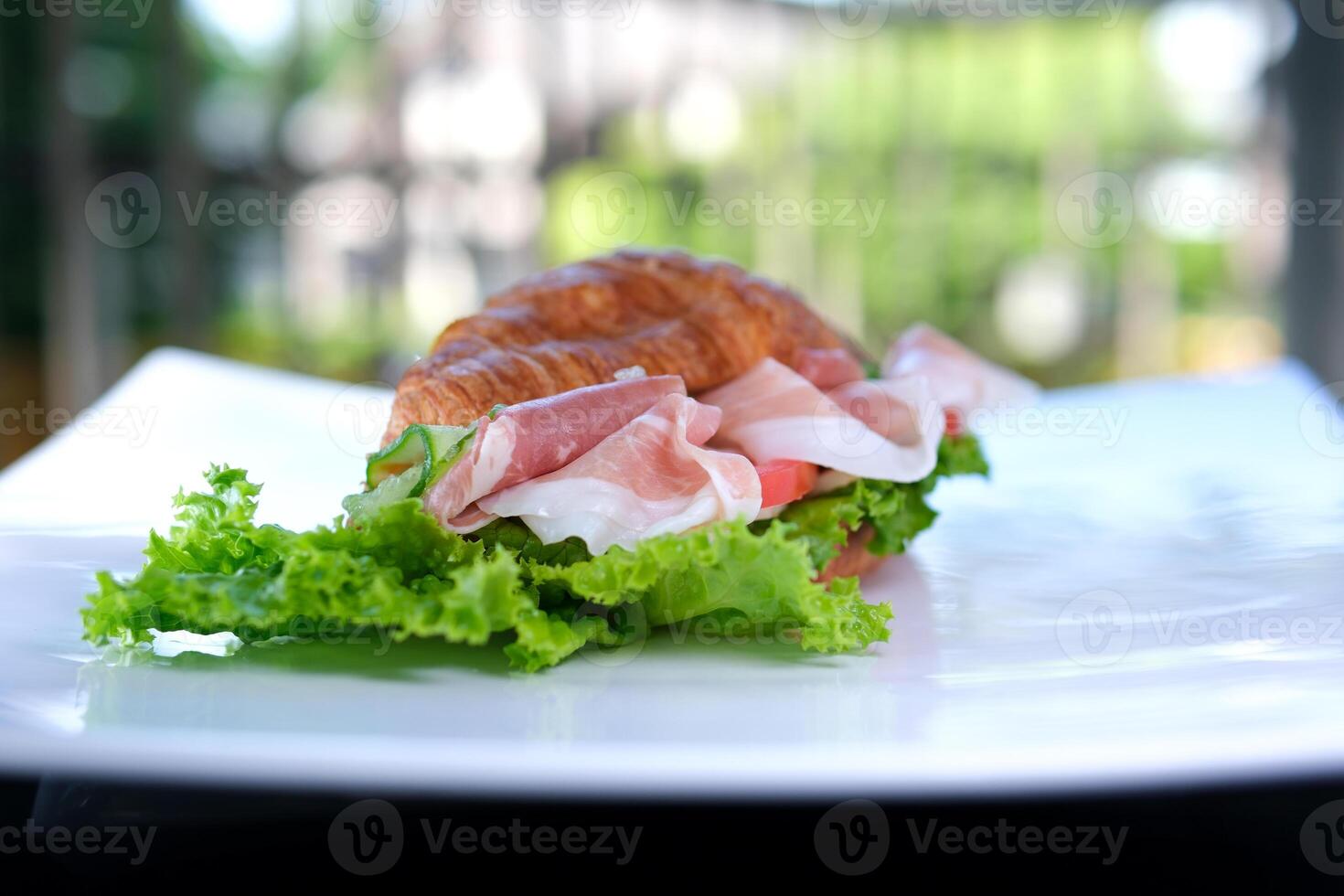 croissant sandwich with meat jamon prosciutto with tomato Lettuce food rich pieces of cheese in breakfast France on a white plate expensive restaurant hotel getting a piece of meat with a fork photo