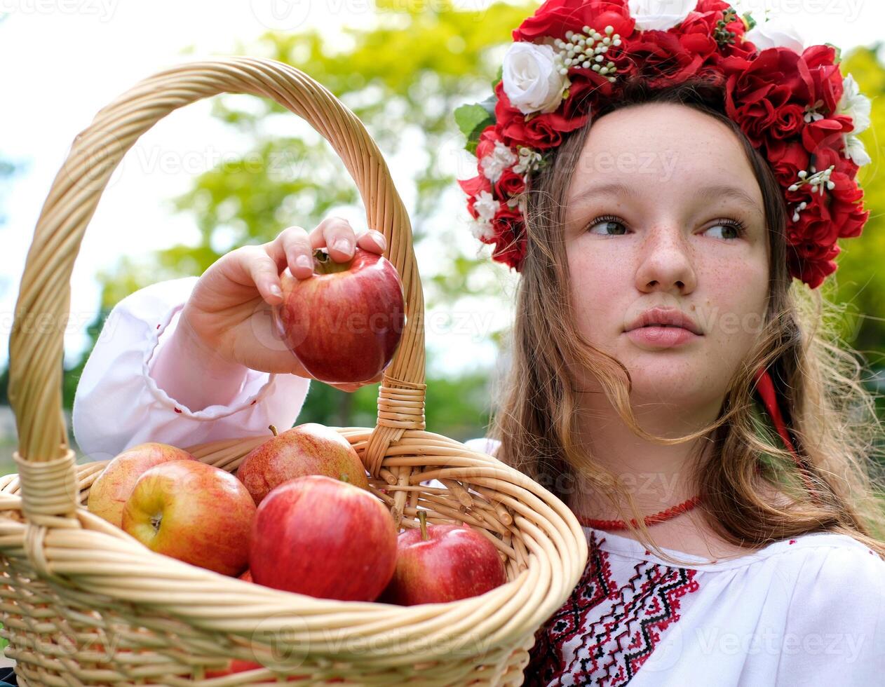 young beautiful girl in red wreath of flowers on her head red poppies in vyshyvanka red apples take an apple with hands inhale smell good weather in garden For world beautiful girls women of the world photo