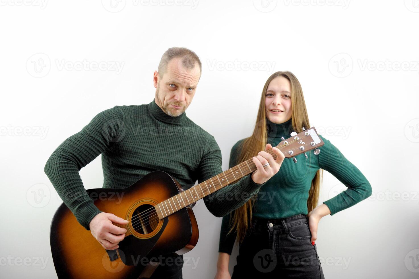 curly man sitting on couch and playing acoustic guitar near happy woman with teddy bear photo