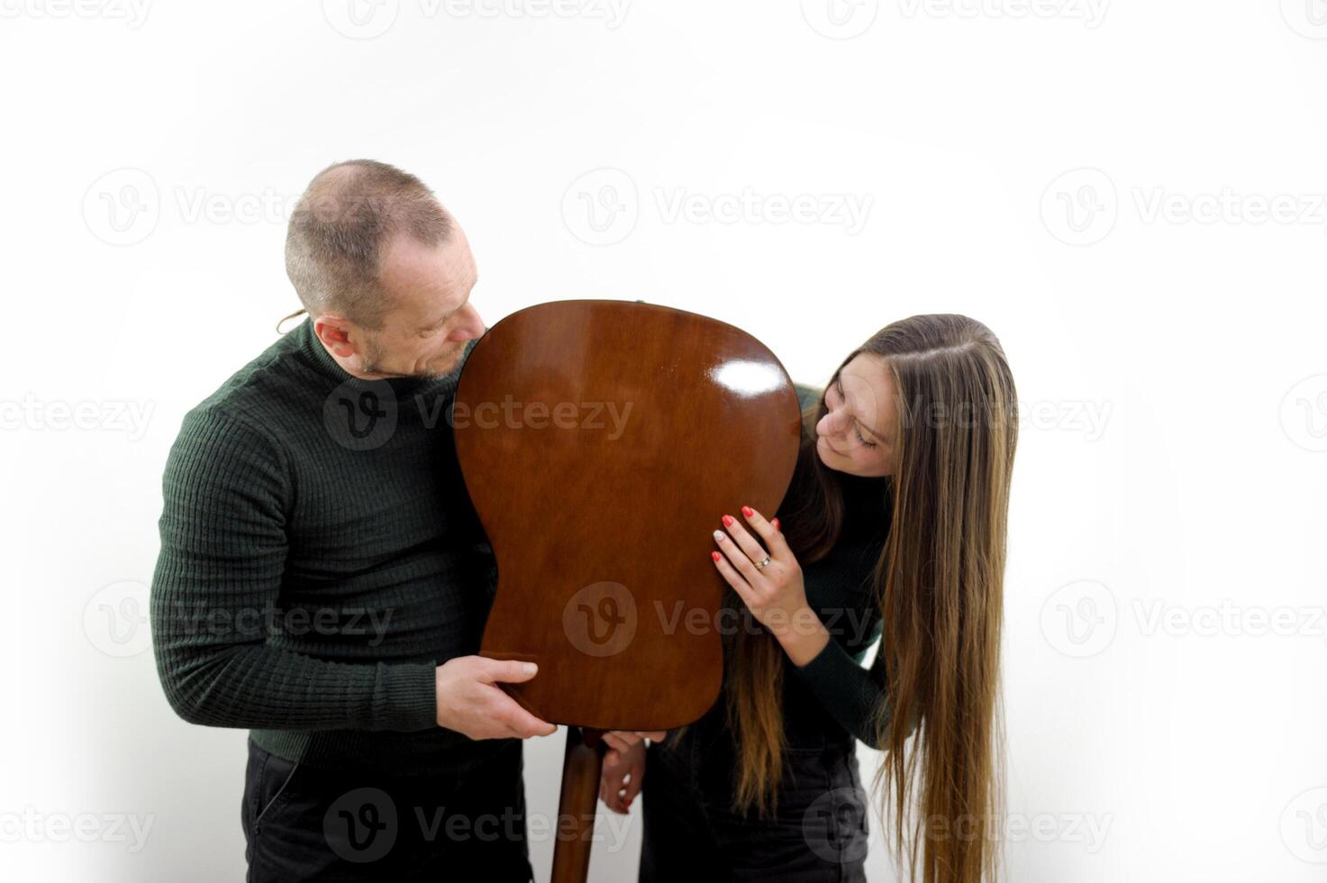 man and woman fooling around with a guitar turned it upside down talking leaning their chin on a white background a couple in love having fun doing a photo shoot laughing posing