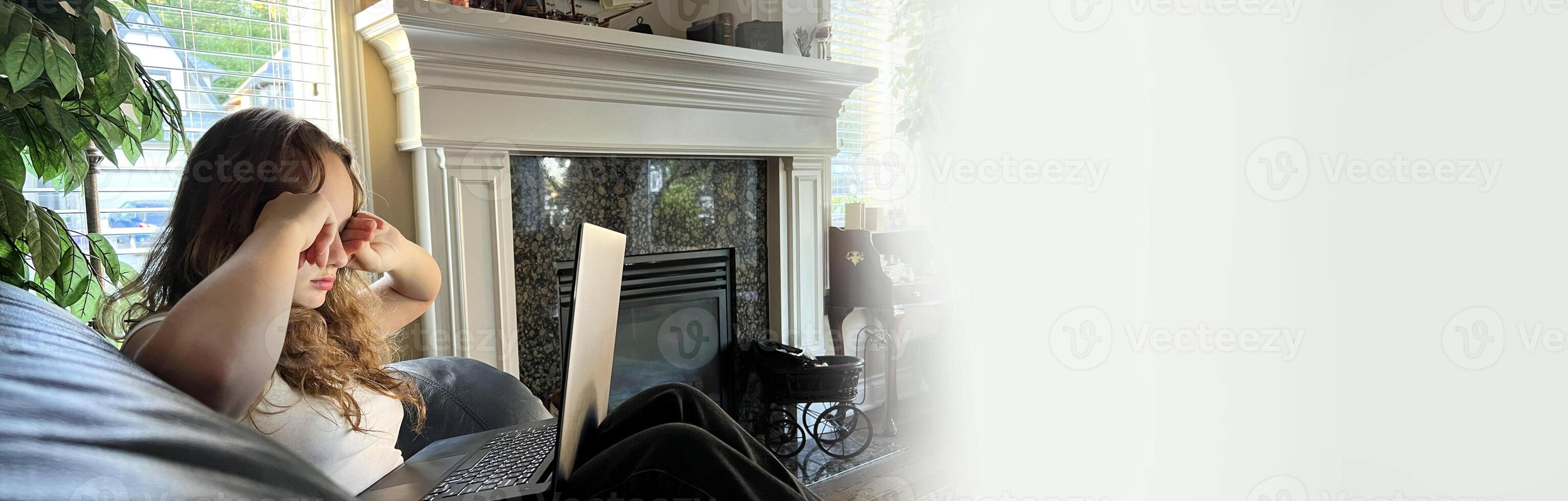 the girl worked at the computer, her eyes are tired, she rubs them with her fists on the front laptop and she on a leather sofa there is a fireplace online training vision improvement of vision photo