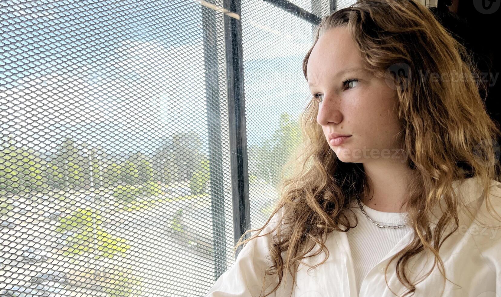 European girl with blond long hair in a white shirt rides in a skytrain she sadly looks out the window she is sad waiting for her A long road outside the window flashes nature houses Vancouver Surrey photo