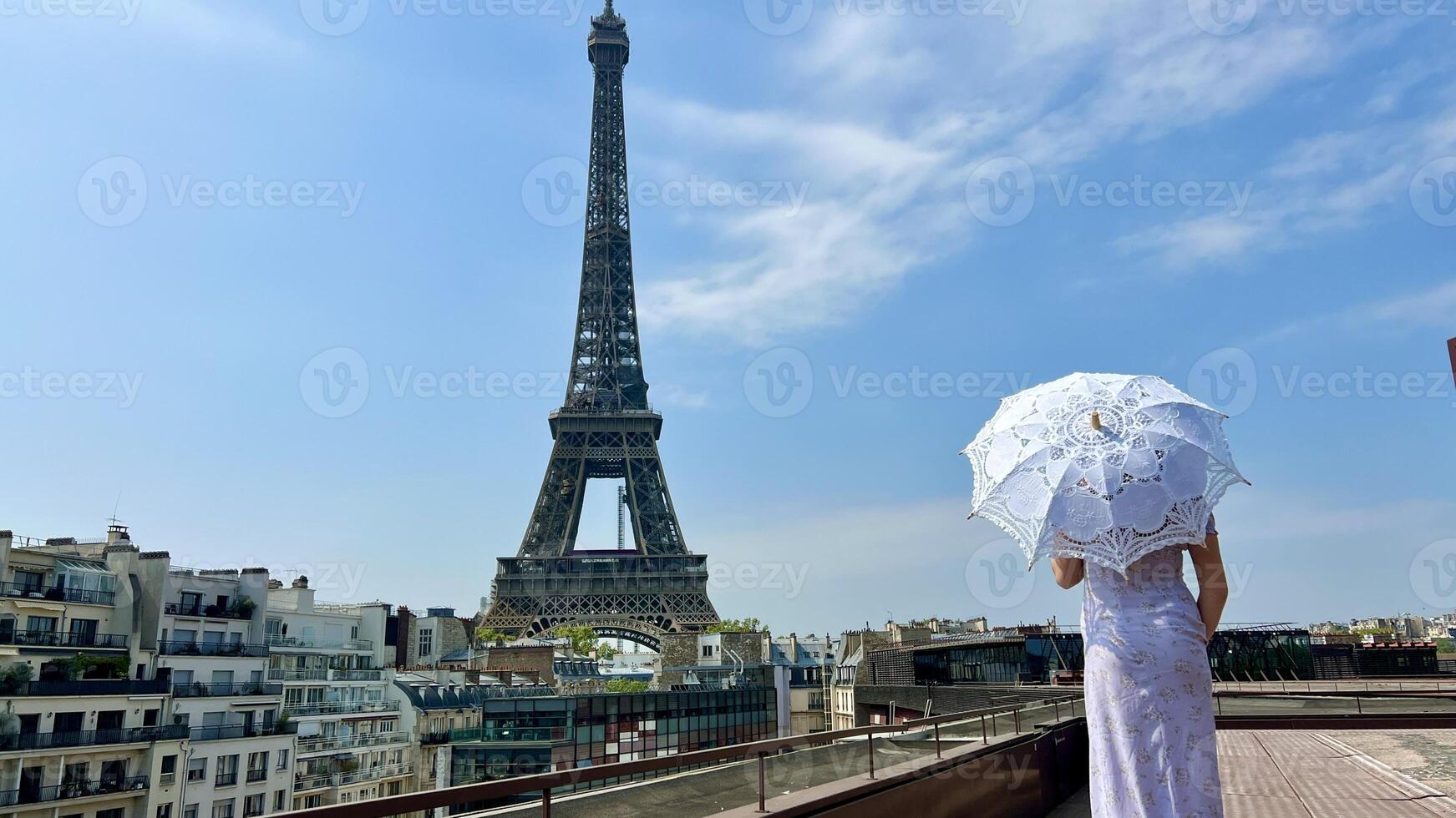 a beautiful young girl in a summer dress stands against the backdrop of the Eiffel Tower with a lace umbrella, she raised her hand and as if taking off there is a place for advertising travel agency photo