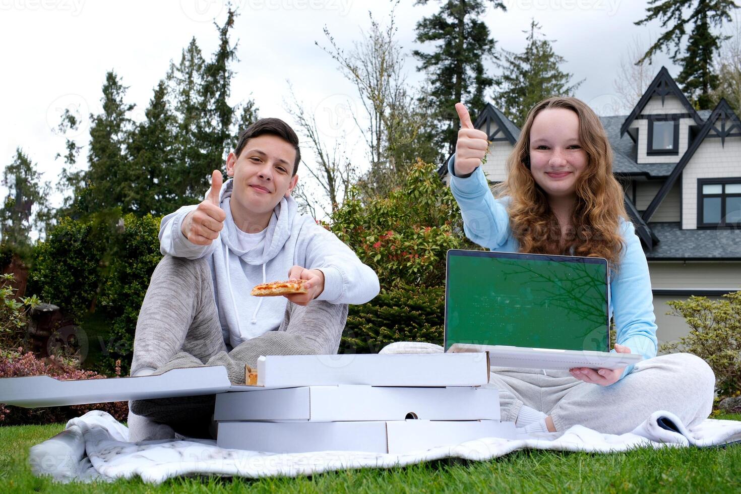 friends ordered pizza to take home laptop with green screen chroma key thumb up open box place for text ad pizzeria sit on grass picnic near house teenagers schoolchildren spend time together photo