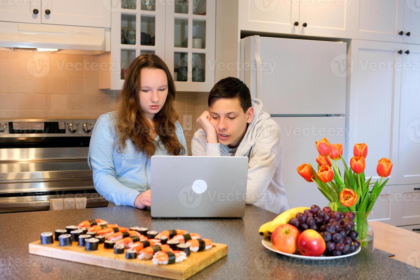 look at laptop lean over focused think look teenagers doing homework in the kitchen ordered sushi meet after school first date watch movie spend time together boy girl 13 14 15 years old photo