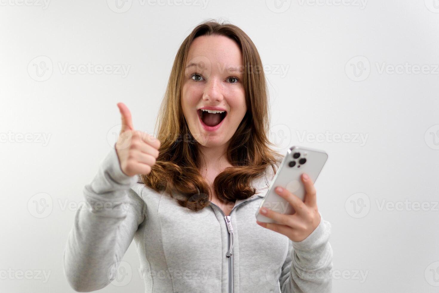 Young happy fun secretary employee business woman in casual shirt work stand at white office desk with pc laptop hold mobile cell phone show thumb up gesture isolated on pastel blue background studio. photo