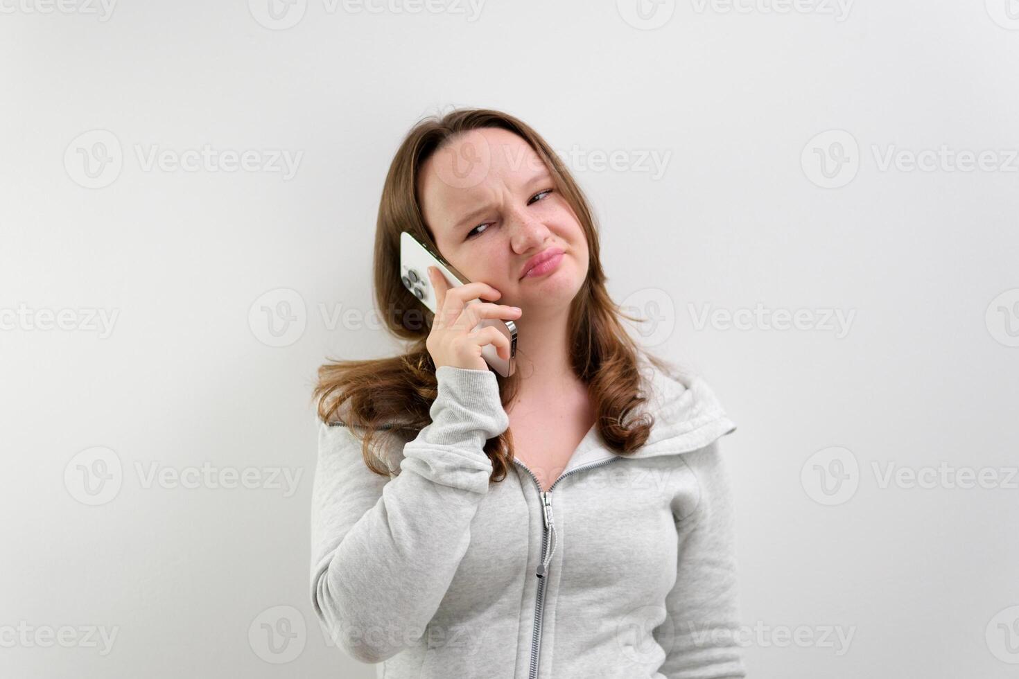 Frustrated annoyed sad woman with mobile phone standing intside white background photo
