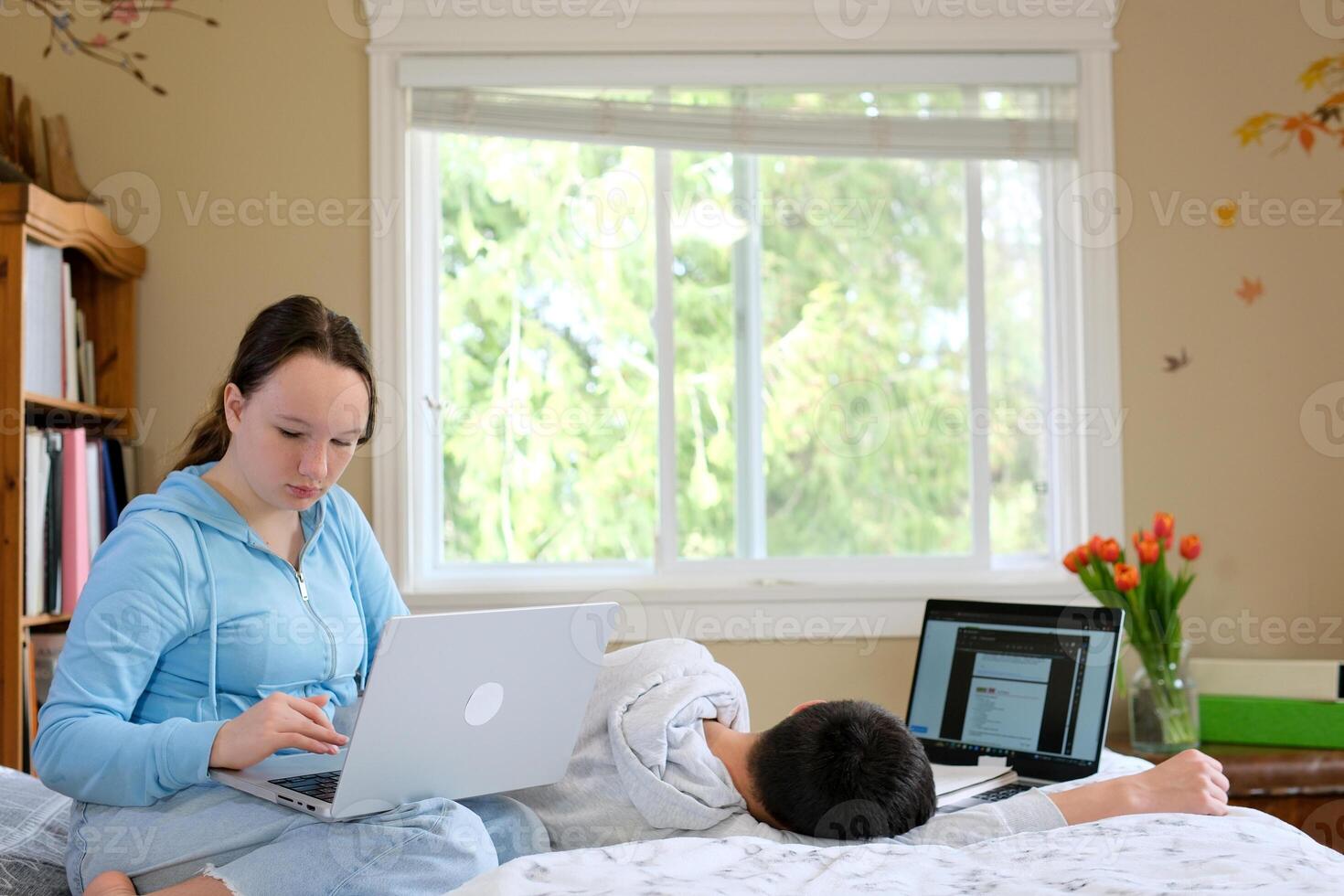 teenagers sit at computers do their homework online study and are not tired of studying go to bed fall asleep One works the other sleeps no desire to study eyes hurt need to rest photo