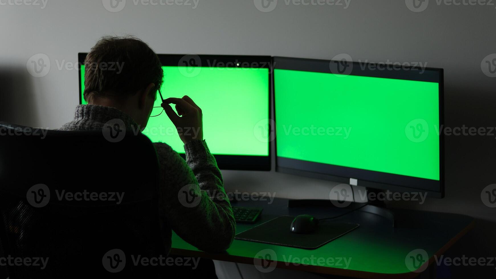 close-up green screens of two monitors man in dark sits with back ad optics space for text online training computer programs fatigue rest time to travel soon weekend working days office weekdays photo