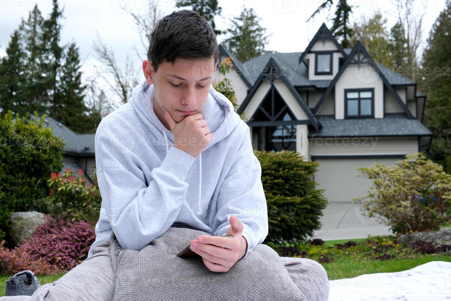 A teenage boy sits on the phone going to his hand in the garden on pillows orders something gadgets phones Communication onlineEducation online School Networks and games for youth and children photo