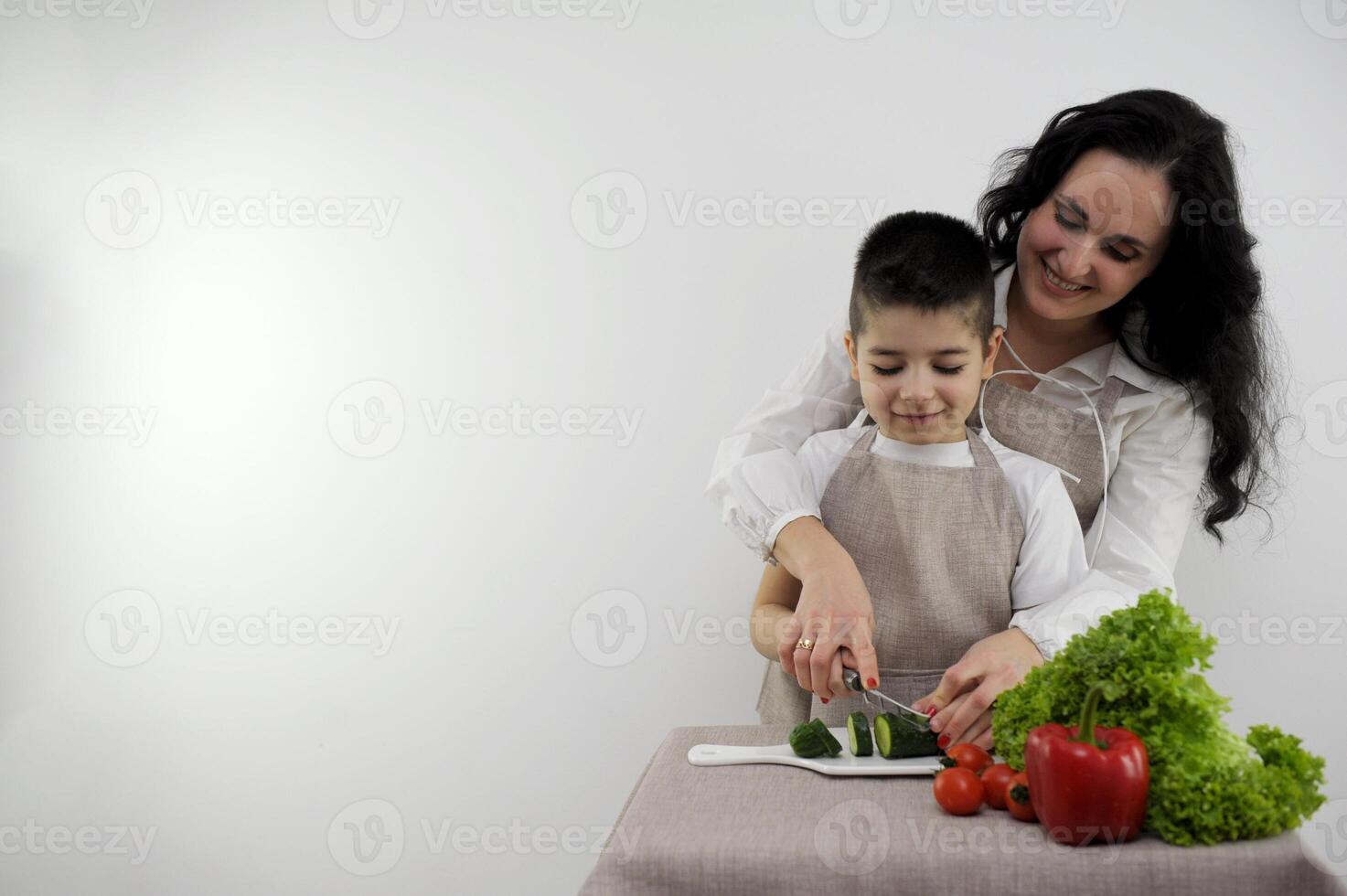 Bonding Concept. Cheerful mother helping her son to cook, teaching little boy how to prepare healthy vegetable salad, cooking together at home. teach a boy to cut cucumber photo