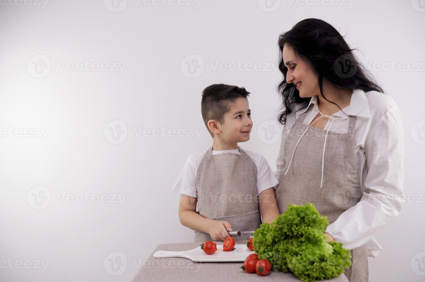 Mom and son cook food in the kitchen together. An adult boy helps mom prepare a vegetable salad. The boy pours olive oil in green vegetables. Healthy lifestyle concept photo