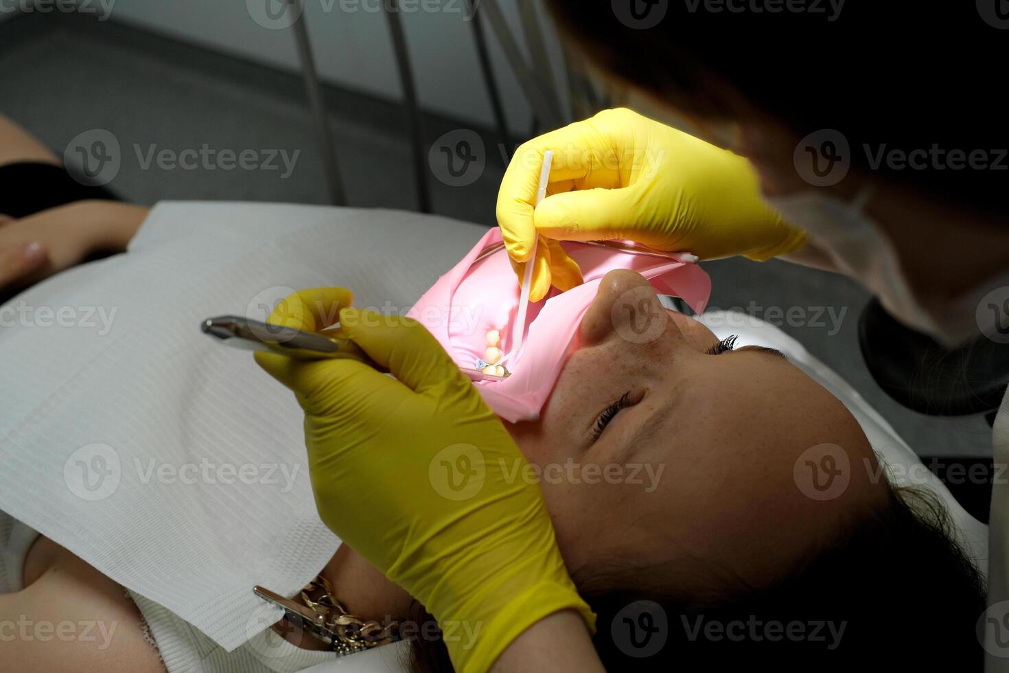 dentistry adolescence a doctor in yellow gloves fills a tooth of a young girl for a woman close-up in dentistry at the dentist drying the tooth with light new technologies modern clinic photo