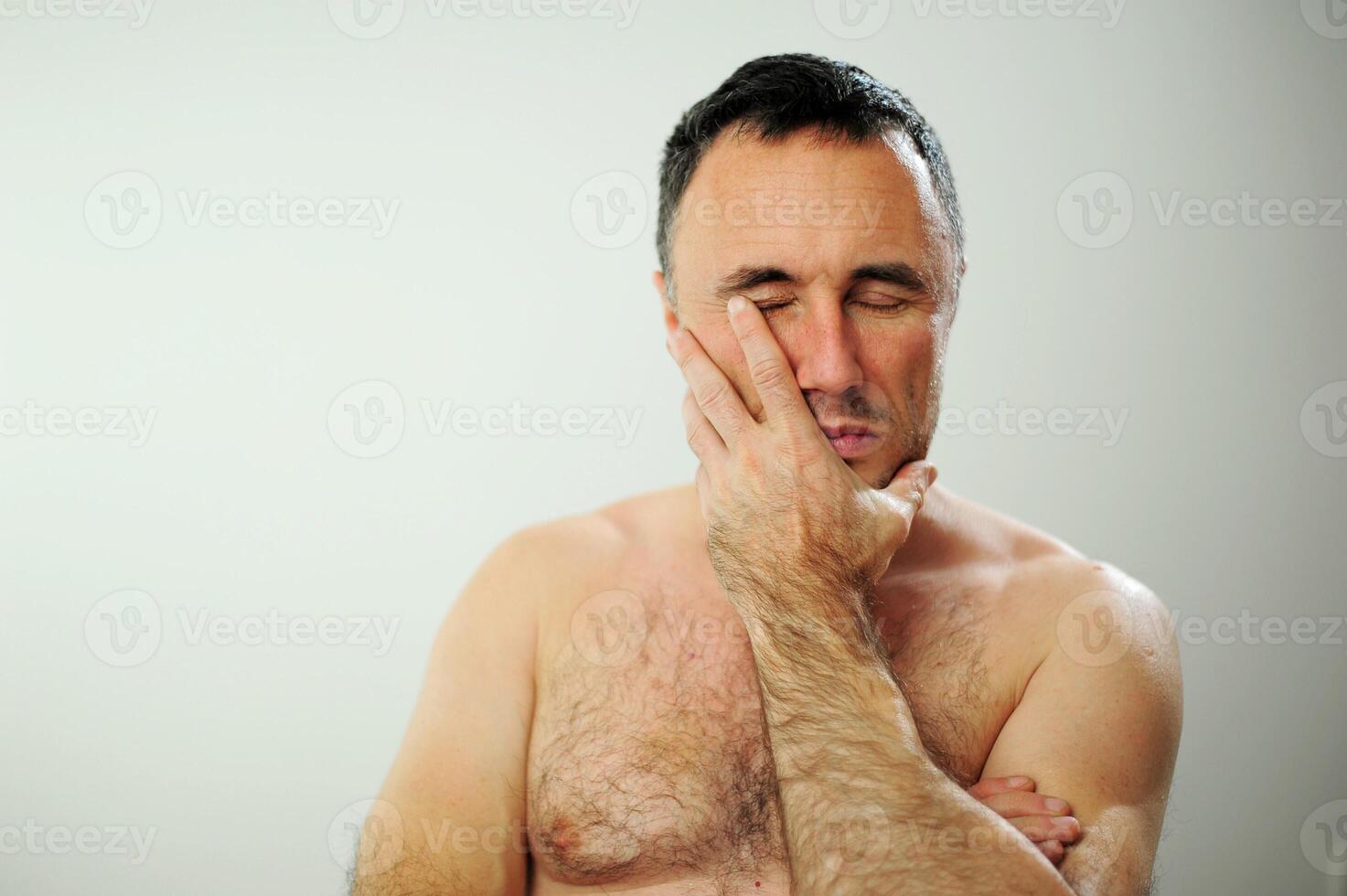 Adult man with naked torso Tired worries thinks about something He has sad tired eyes blue green color He stands on a gray background waist-deep close-up When will it end when will the best time come photo