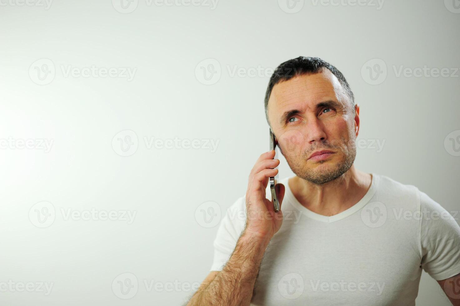 Adult strict man talking on the phone He is angry and a little dissatisfied with the conversation Studio all white phone t-shirt and iPhone space for text white background photo