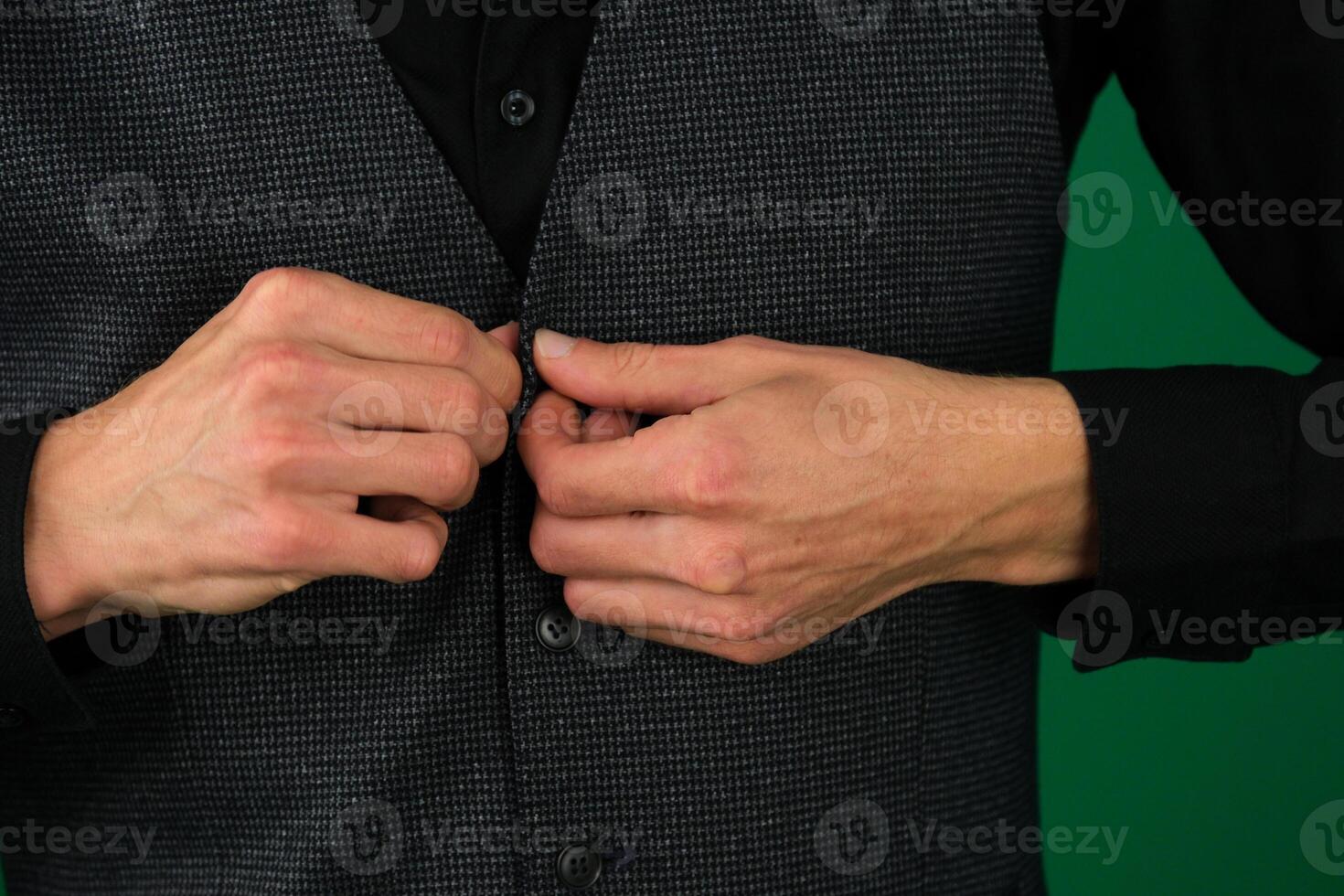 close-up photo of the hands of a man in a black shirt, buttoning up a button on green background
