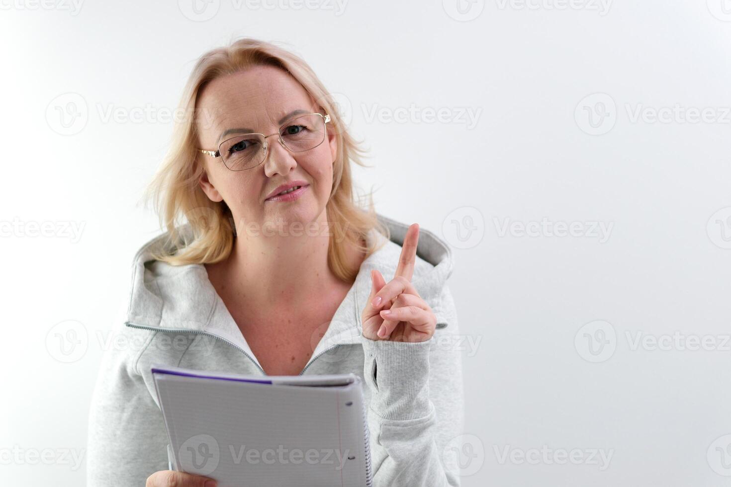 the teacher points with her finger at a notepad with her mouth open glasses on a blonde beautiful people to attract attention instructions look here Pay attention to this item manager photo