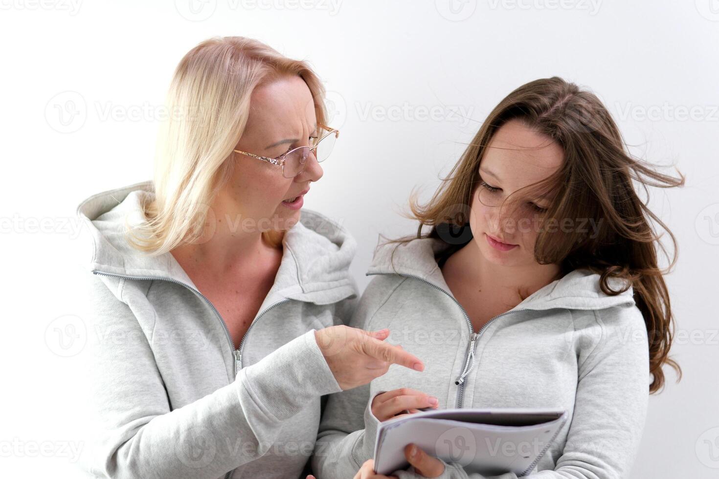 mom and daughter doing homework, woman wearing glasses, girl trying to write, they are laughing, smiling, spending pleasant time, explaining to child, surprise, pointing with hand at notepad, notebook photo