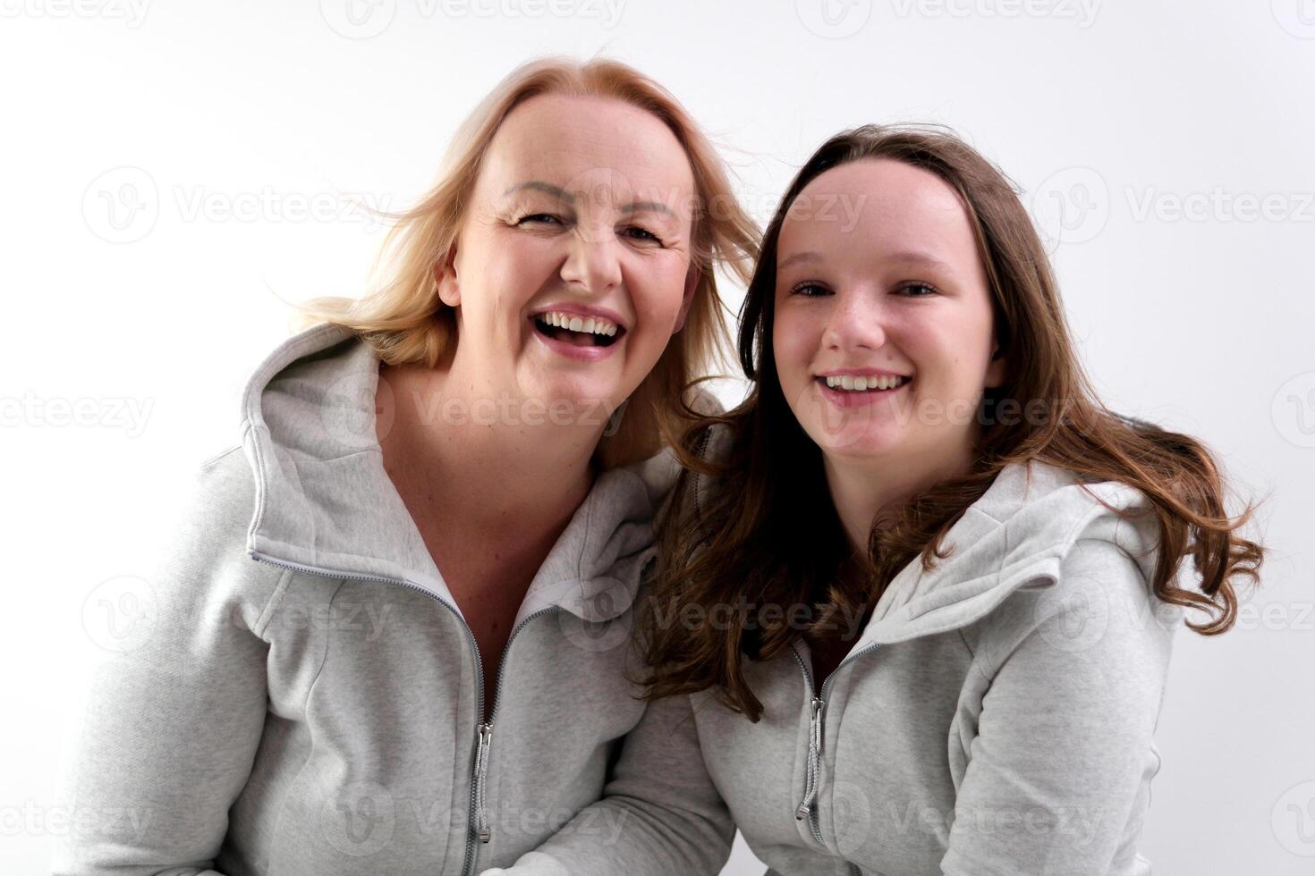 a woman and a girl hugging leaning their cheeks against each other look into the frame pull lips for kiss mom and daughter on white background identical clothes close eyes from pleasure tenderness joy photo