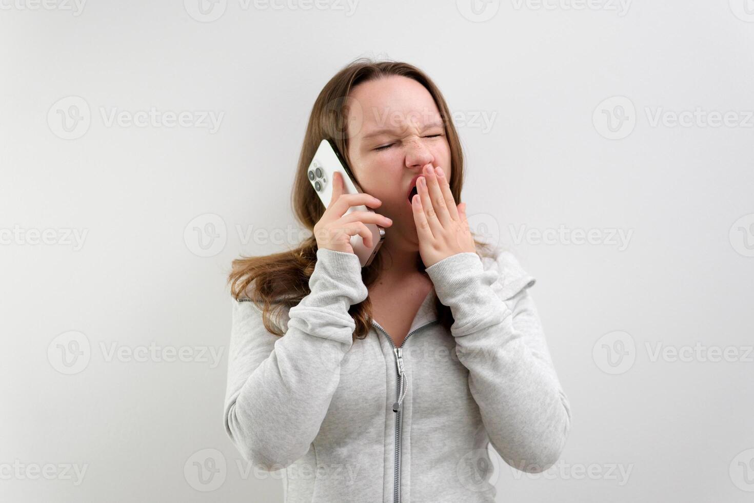 Young woman in light green sweater with mobile phone having conversation listen audio message bored tired sleepy yawning photo