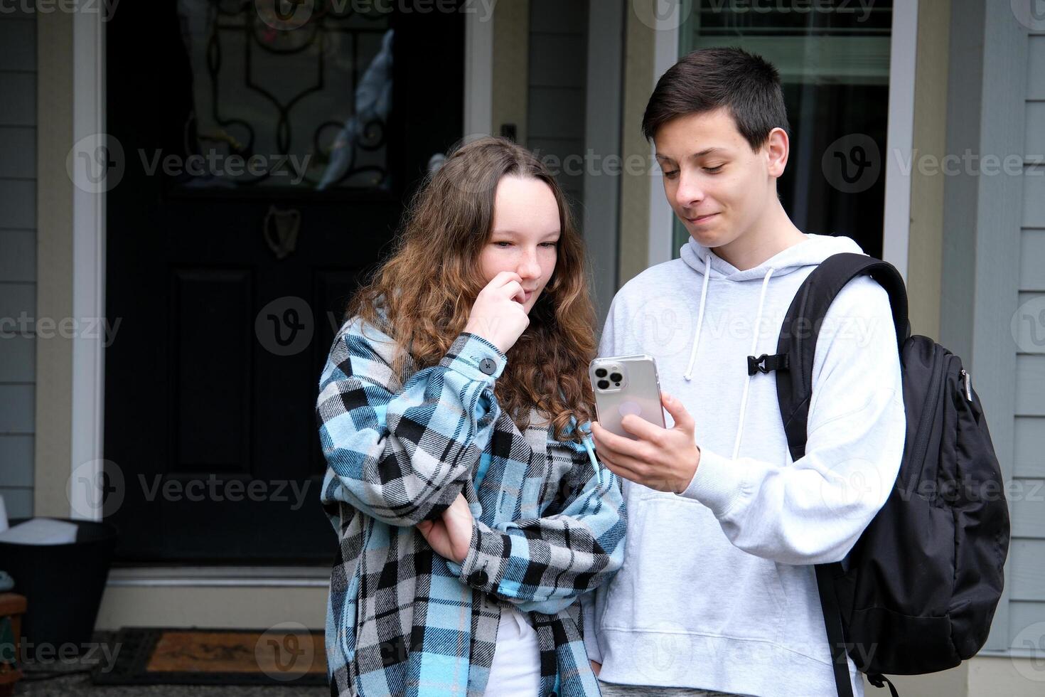 teenagers show interesting news boy and girl with briefcase phone at door at home Smiling couple looking in smartphone together. Beautiful loving couple laughing and watching something on mobile phone photo