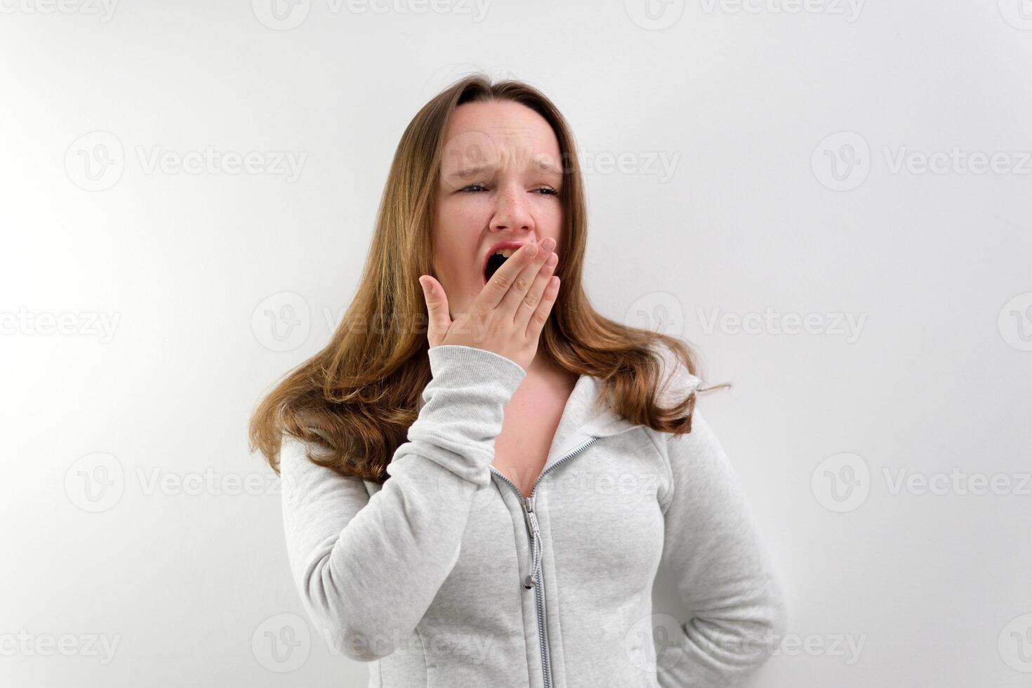 tired yawning in the frame teenage girl tired of studying to work talking yawning with her mouth open covering her face with her hand beautiful hair well-groomed boring life in the studio photo
