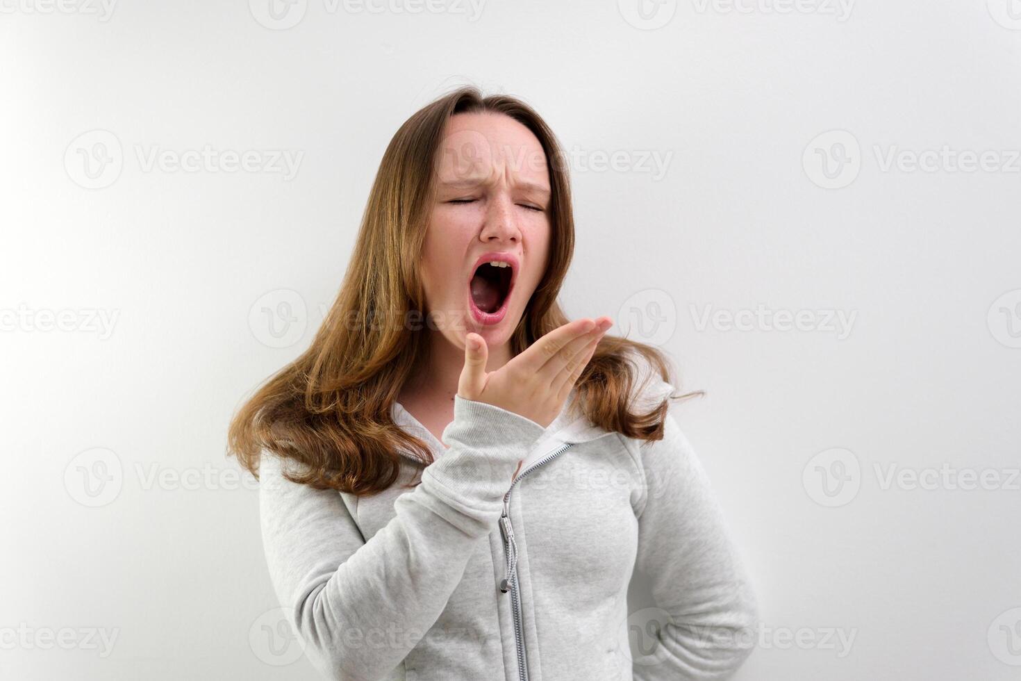 tired yawning in the frame teenage girl tired of studying to work talking yawning with her mouth open covering her face with her hand beautiful hair well-groomed boring life in the studio photo