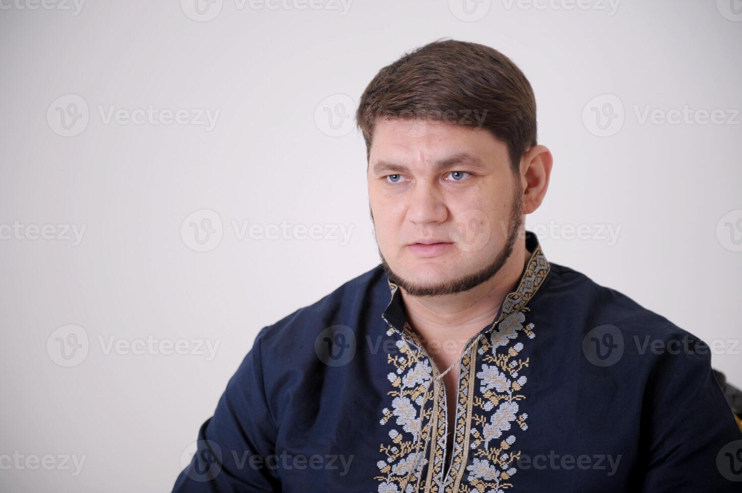 Waist-up shot of serious-looking unemotional good-looking adult man in gray t-shirt looking at camera calm and strict, being snob and hard to impress standing over gray background. photo
