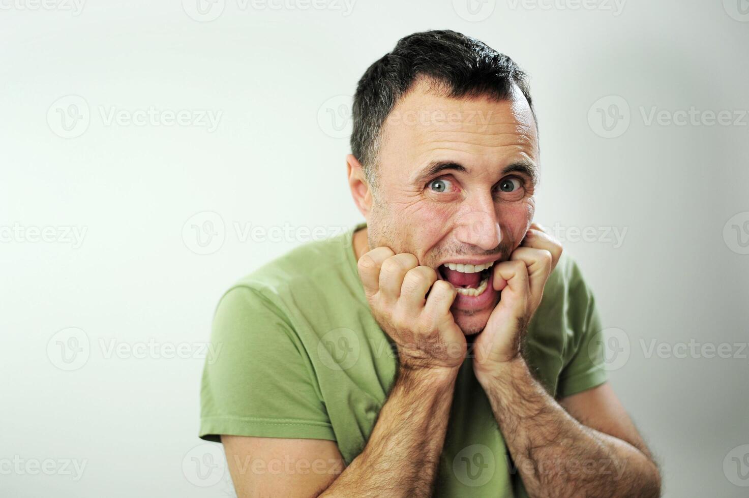sly funny look adult unshaven man tears Green khaki T-shirt and bites his fingers 40-49 years Black hair at the temples gray Experience stress upset neurosis Studio white background photo
