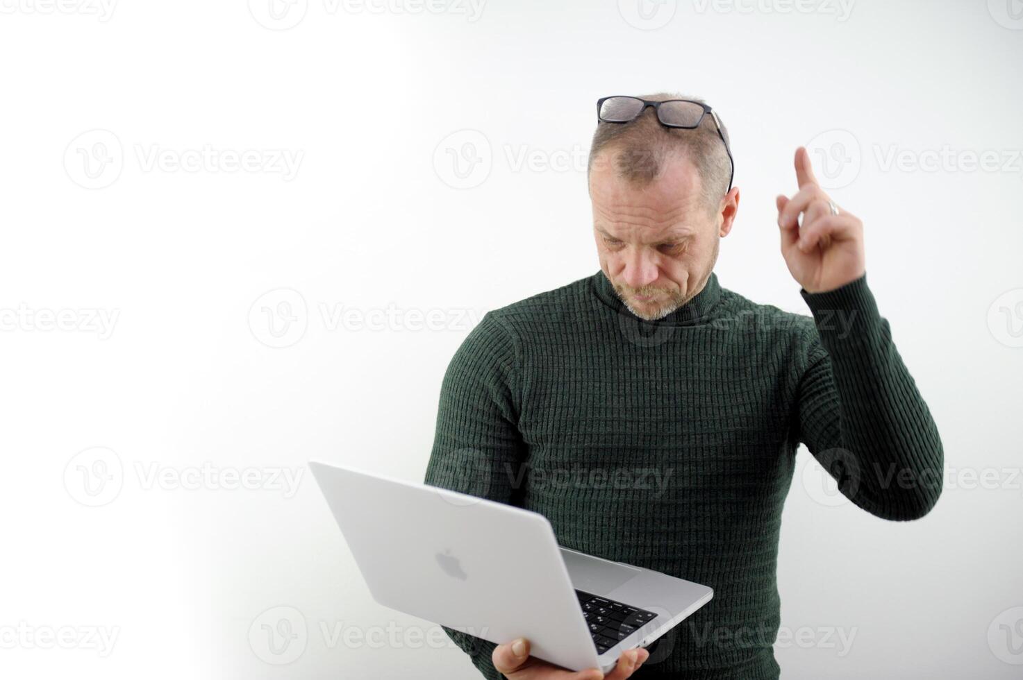 a man in a green sweater, an adult, raised his finger up, put glasses on his forehead, looks in surprise at a laptop on a white background Student using laptop isolated on white photo