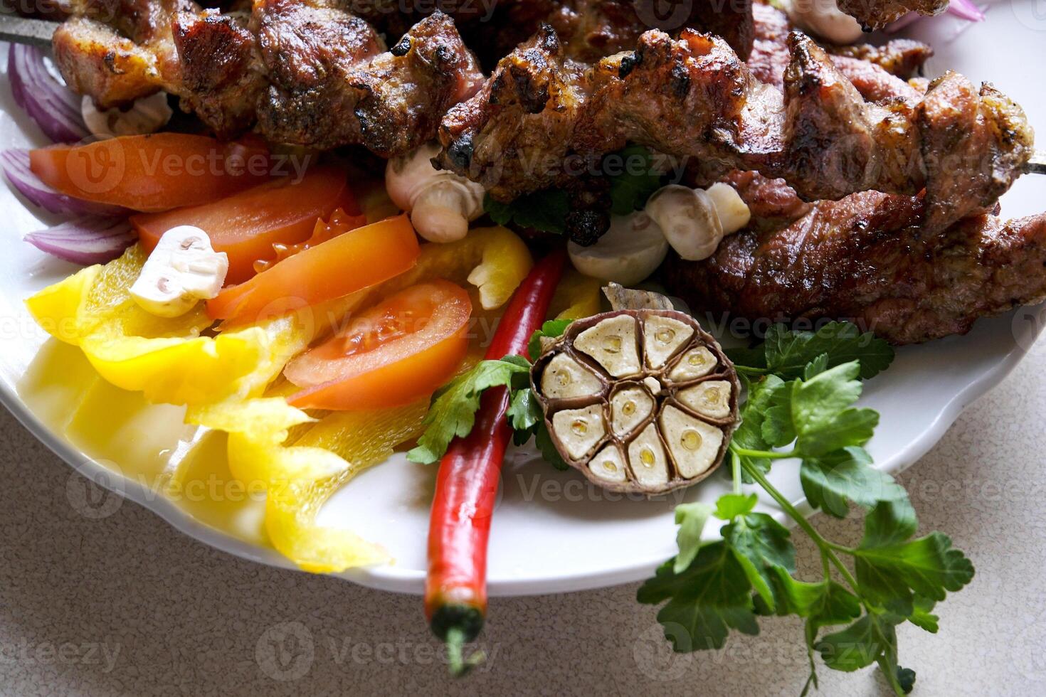 Shashlik or shish kebab prepared on barbecue grill over hot charcoal with grilled vegetables. Grilled pieces of pork meat on metal skewers. photo