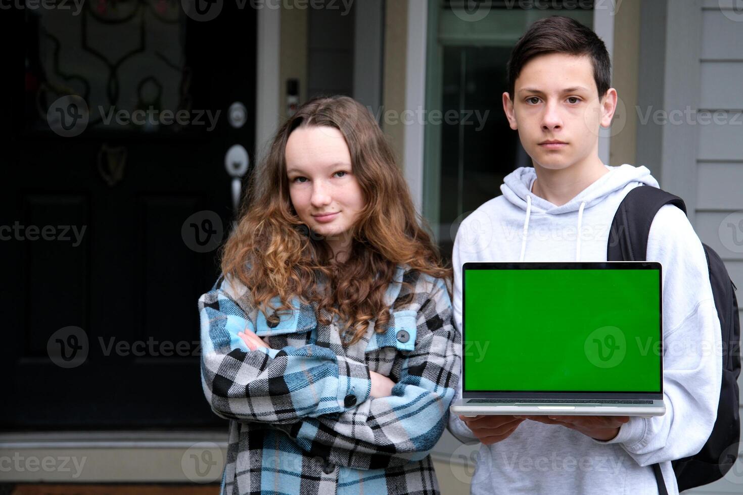 serious teenagers stand with laptop and backpack schoolbag show green screen chroma key on laptop autumn spring study stand near home advertise online learning language courses boy and girl photo