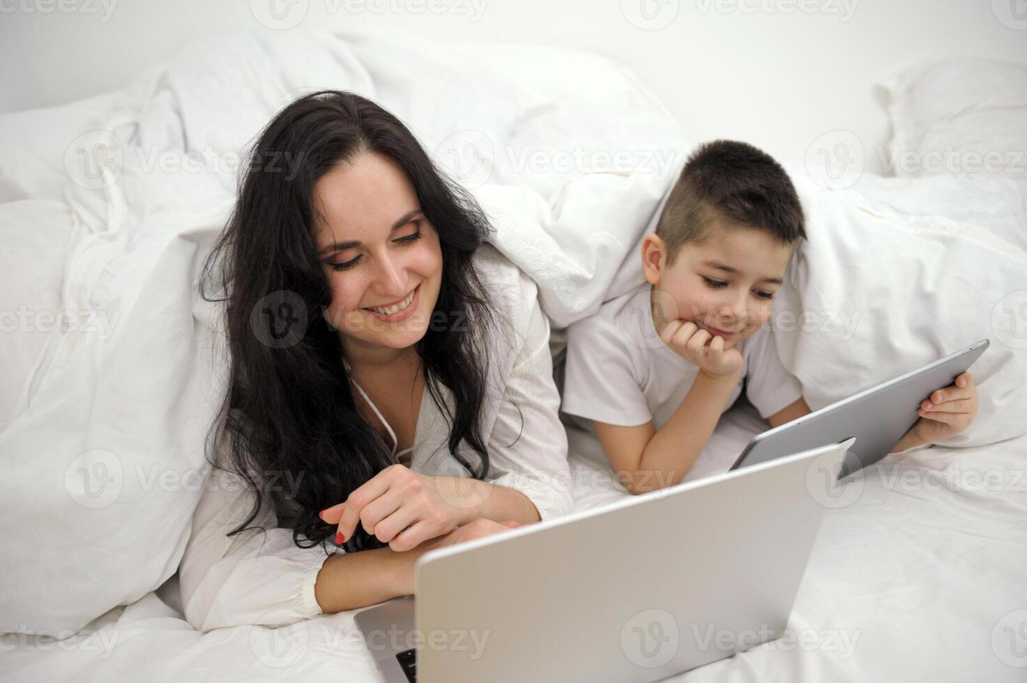 boy, And his mother is working on a laptop computer, The little boy put the tablet in his hand and turned to his busy mother intently, wanting his mother to pay attention to him. photo