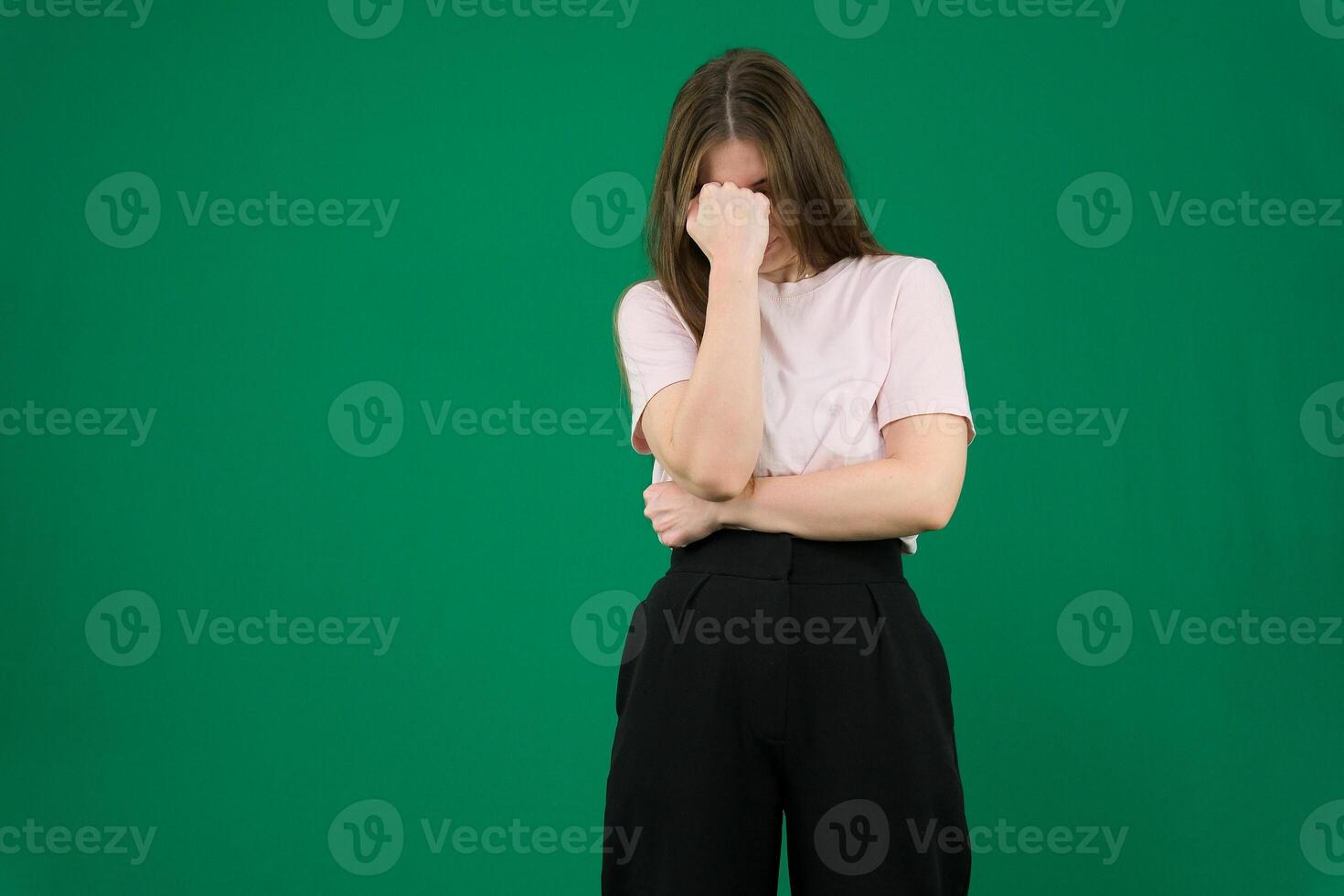sad expression covering face with hands while crying. Depression concept. girl on chromakey beautiful facial features real people pink T-shirt white skinned European. black flared wide leg trousers photo