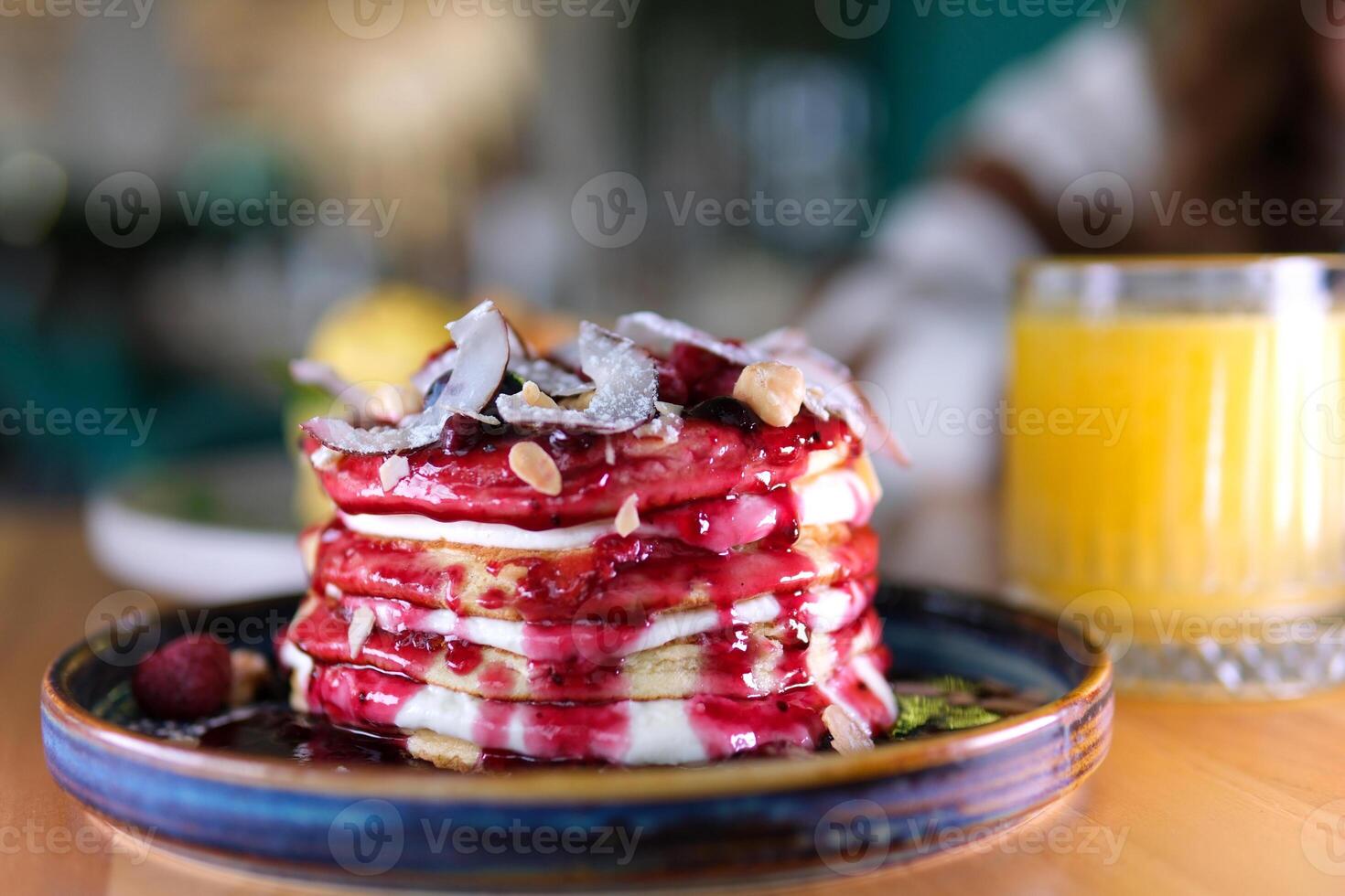 stack of delicious pancake decorated with coconut flakes blueberries hazelnuts almond flakes raspberries and jam delicious breakfast with sour cream eaten with fork in restaurant beautiful serving photo