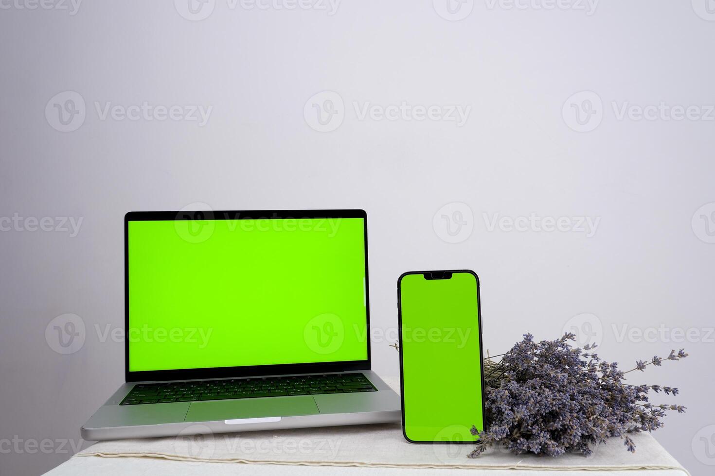 blank mobile phone while using laptop with blank green screen on table Mockup image of Laptop mobile blank green screen in vertical position isolated on green background, Concept device mockup. photo