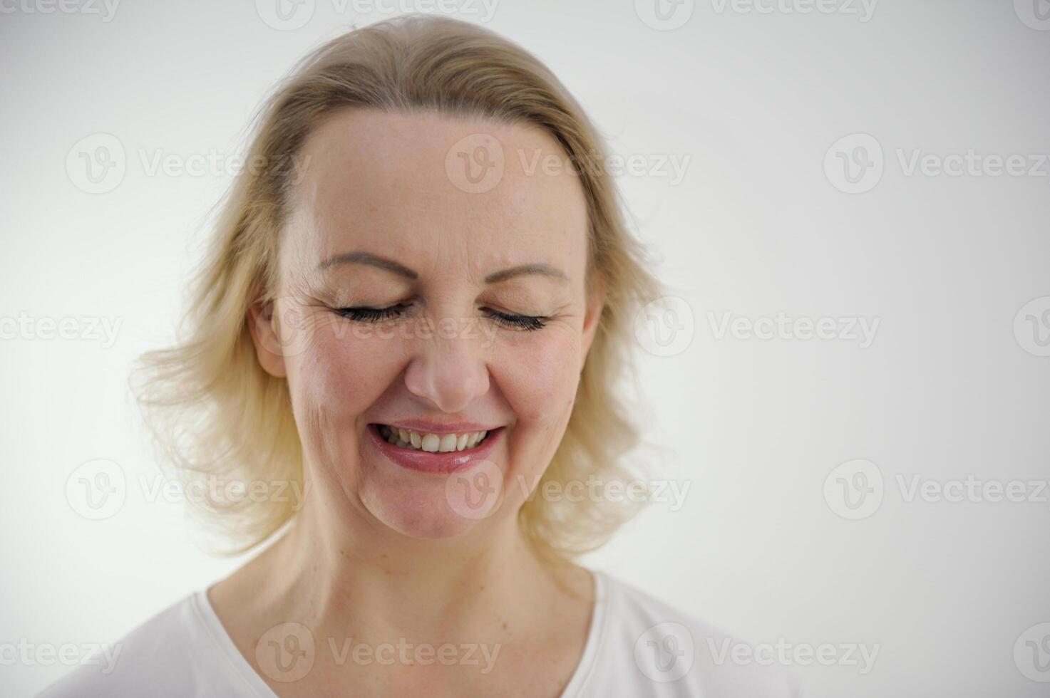 face of a middle-aged woman with blond hair on a white background close-up she lowered her eyes sincerely smiles embossed doubt joy tenderness beauty calmness peace photo