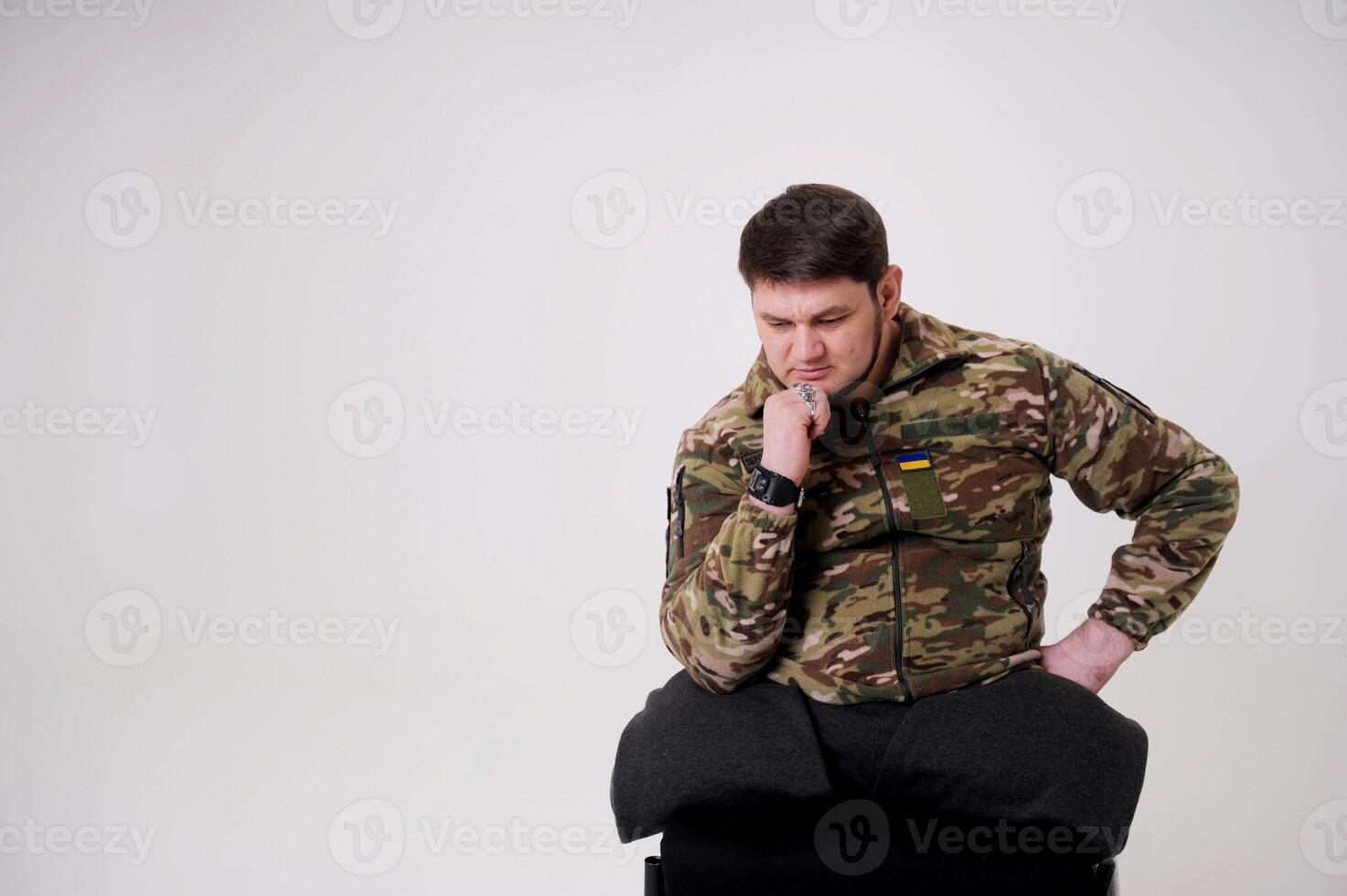 portrait of a male in camouflage coat on gray background Studio shot of young bearded ukrainian man Military serviceman at home having post traumatic stress syndrom photo