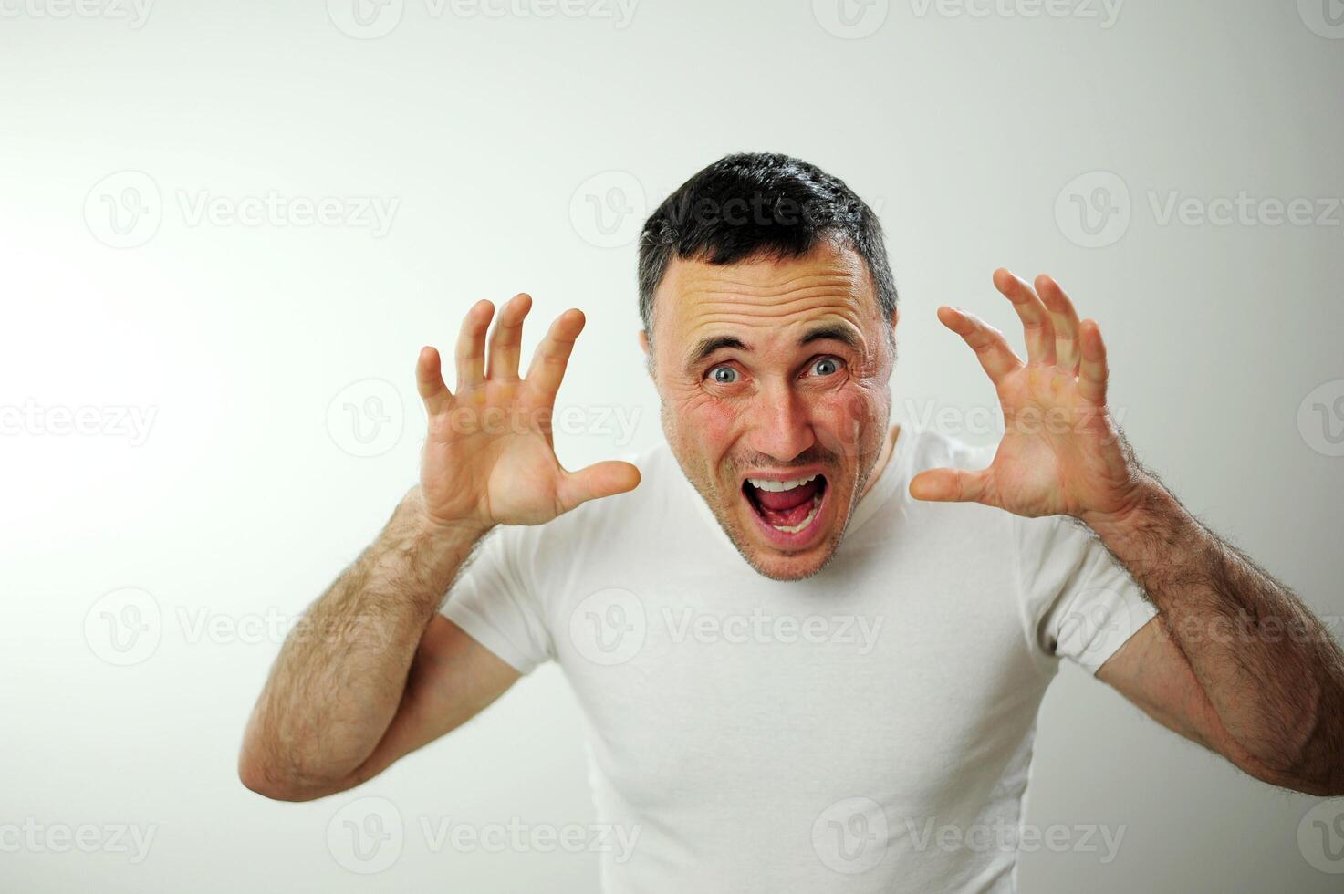A middle-aged man with kind eyes as if trying to scare someone, spread his fingers and opened his mouth and looks into the frame he is funny Usually scare children so that they hide and laugh photo