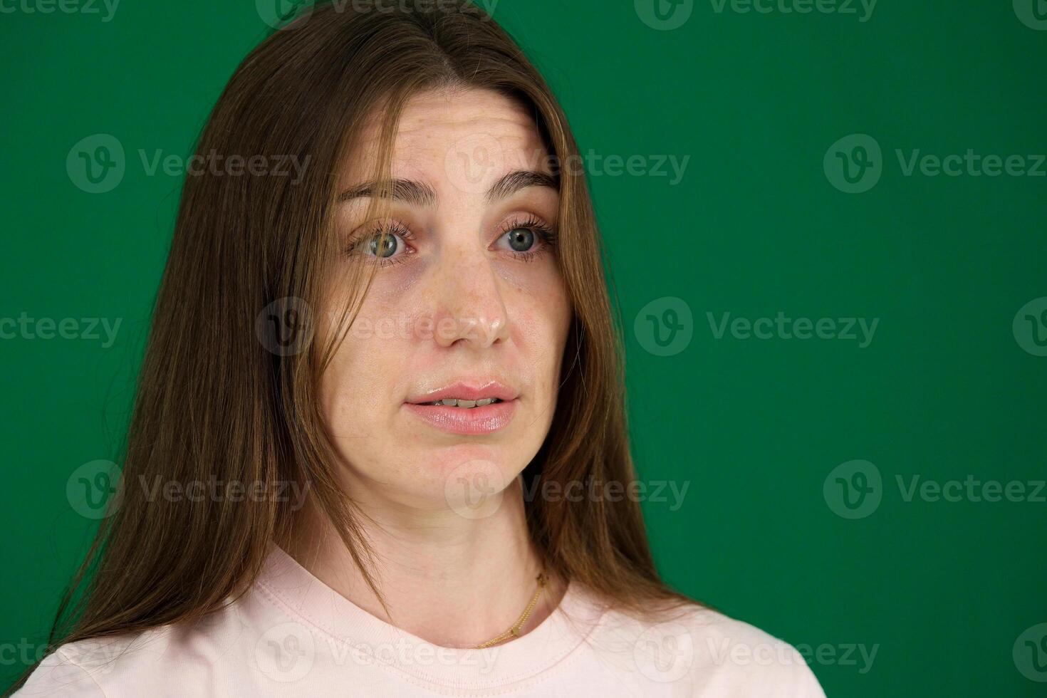 Close up portrait of angry redhead teenage girl. different emotions of a young girl on a green background chromakey beautiful facial features real people pink T-shirt white skinned. European photo