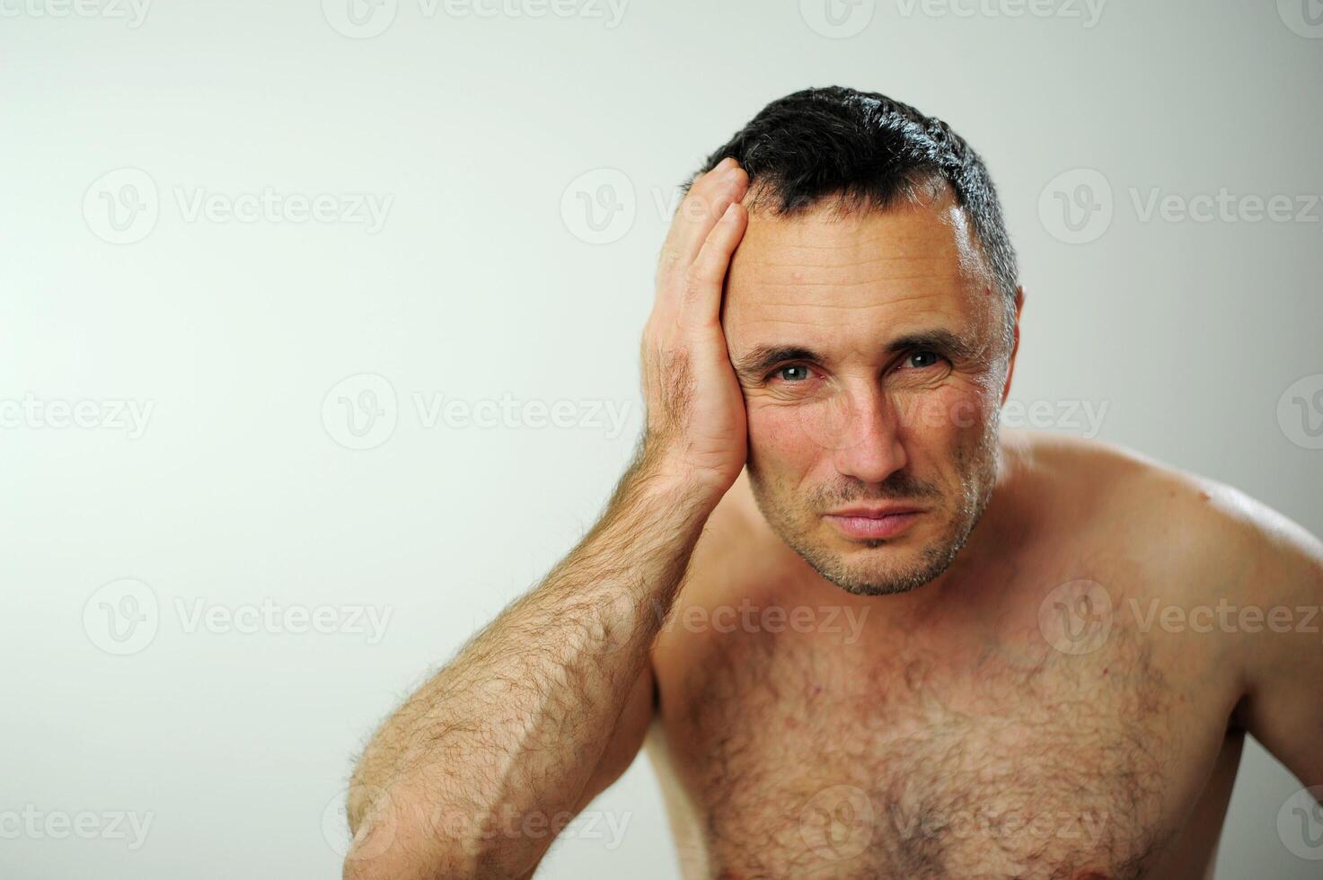 Adult man with naked torso Tired He has sad tired eyes man in the bathroom Looks in the mirror directly at us He is naked with a naked torso he has a hairy chest hairy arms surprise handsome man photo