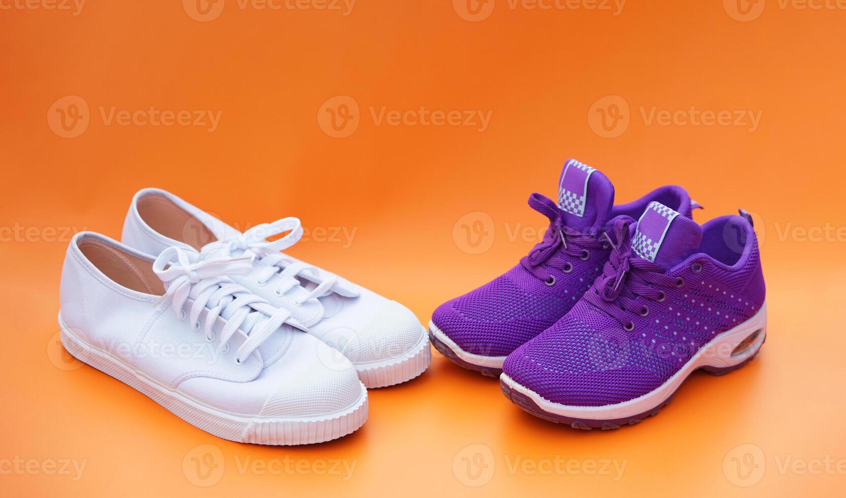 Two pairs of white and purple canvas sneakers. Orange background. Comfortable, fashionable. Concept, shoes for doing sport or exercise also can wear for traveling, hiking. photo