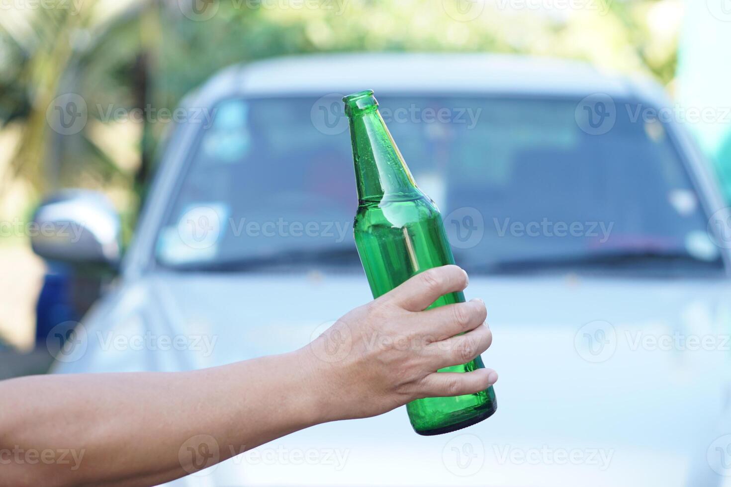 Close up hand hold bottle of beer, Outdoor, blurred car background. Concept, Stop driving while drinking alcohol beverage or whiskey campaign. Illegal, dangerous to drive vehicle that lead to accident photo