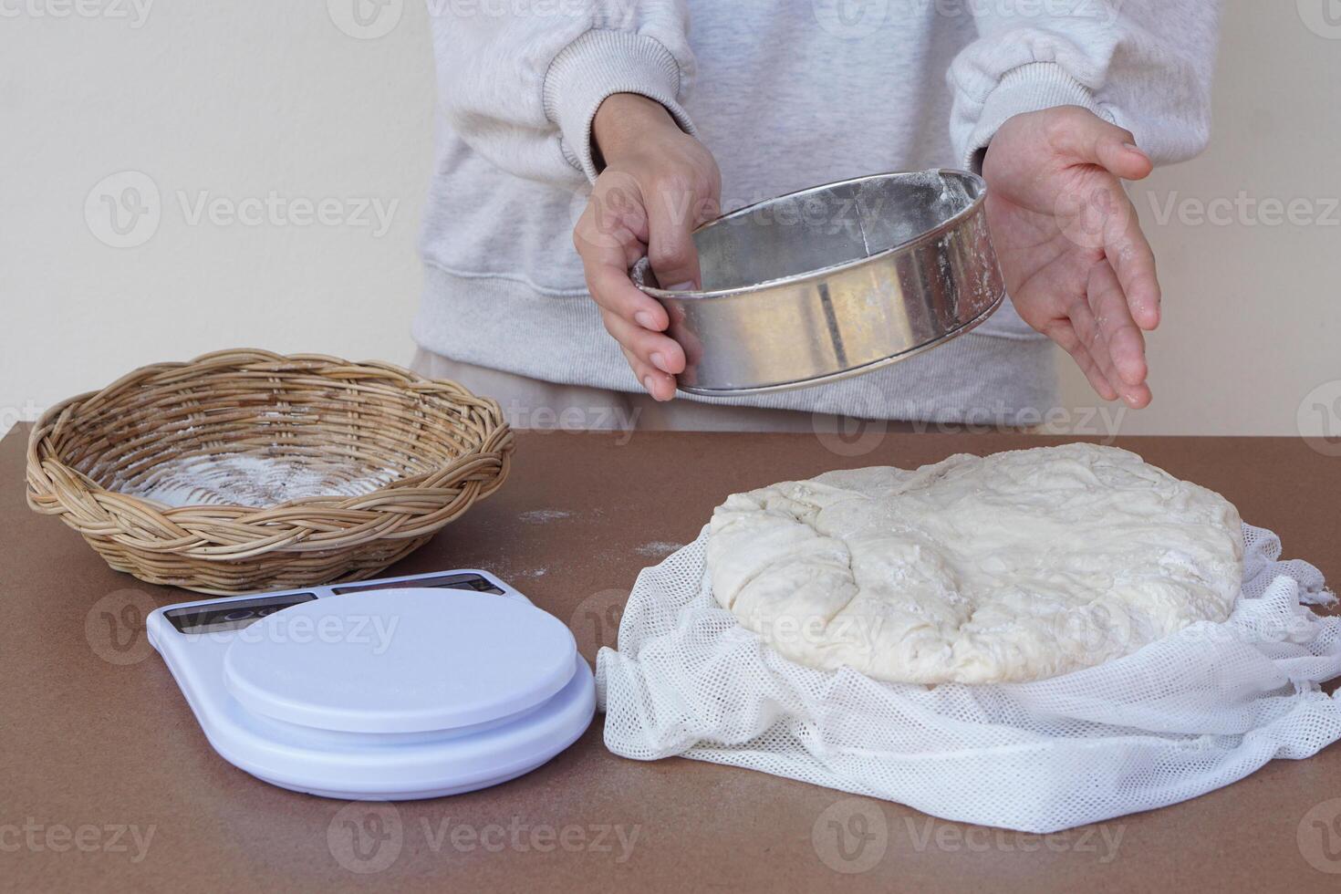 Close up hands holds stainless flour sieve to prepare dough to make bread or pizza. Basket, scale on cooking table. Concept, cooking. Kitchen lifestyle. Preparing food. Bakery. Love cooking. photo