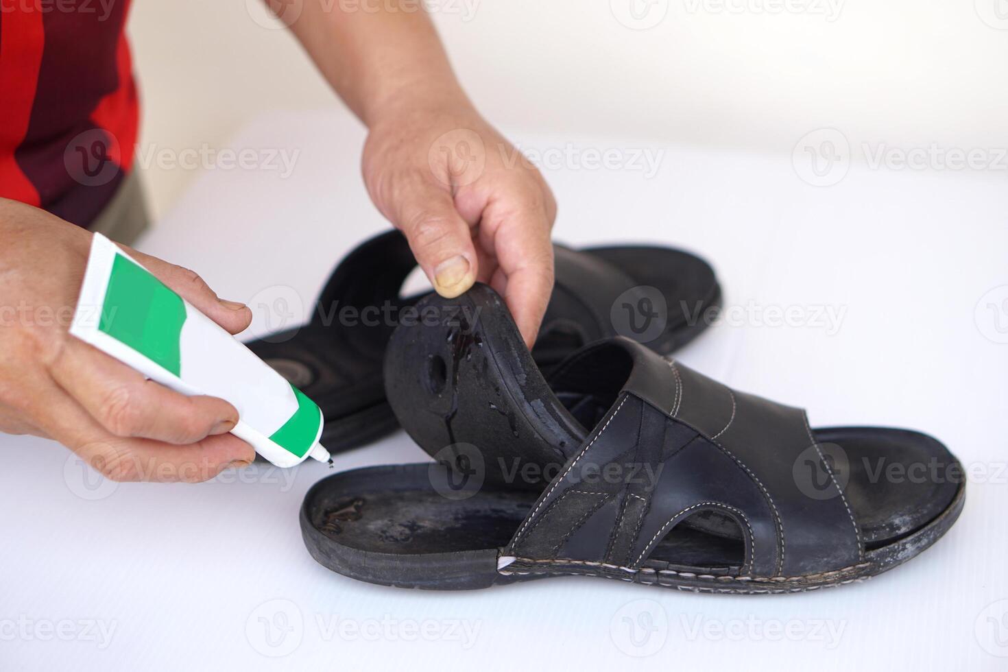 Closeup man hand use super glue to fix broken shoe. Concept, repair for reuse or recycle footwears before being garbage. photo