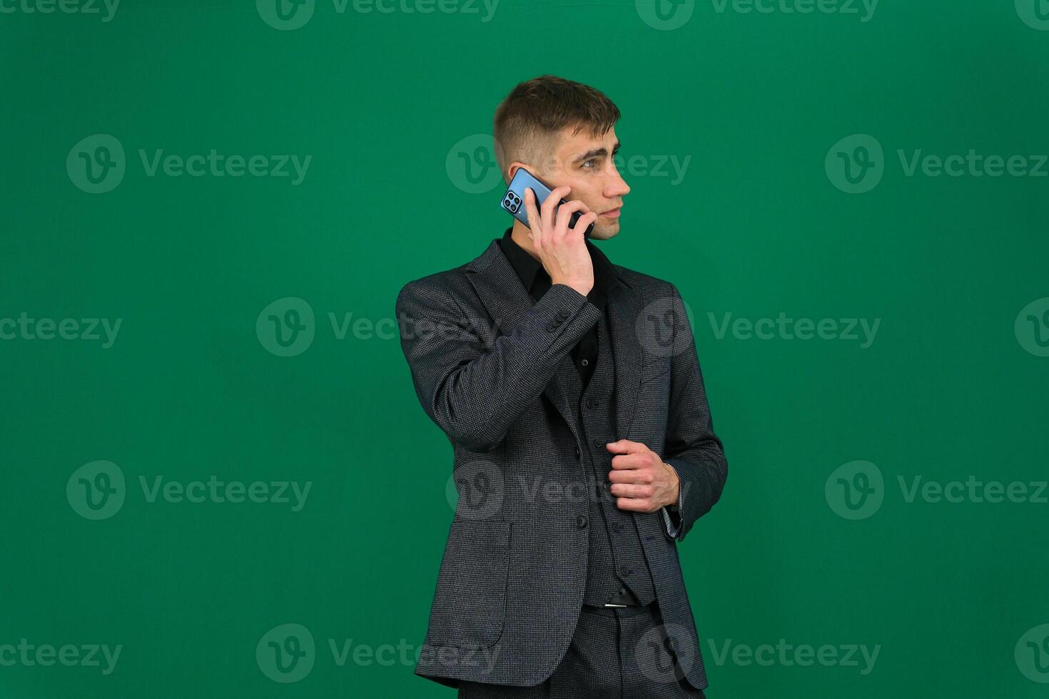 A man vaping in formal suit emotions of a handsome man guy on a green background chromakey close-up dark hair young man. phone in hand talk dial SMS online call gadget boss work advertising photo