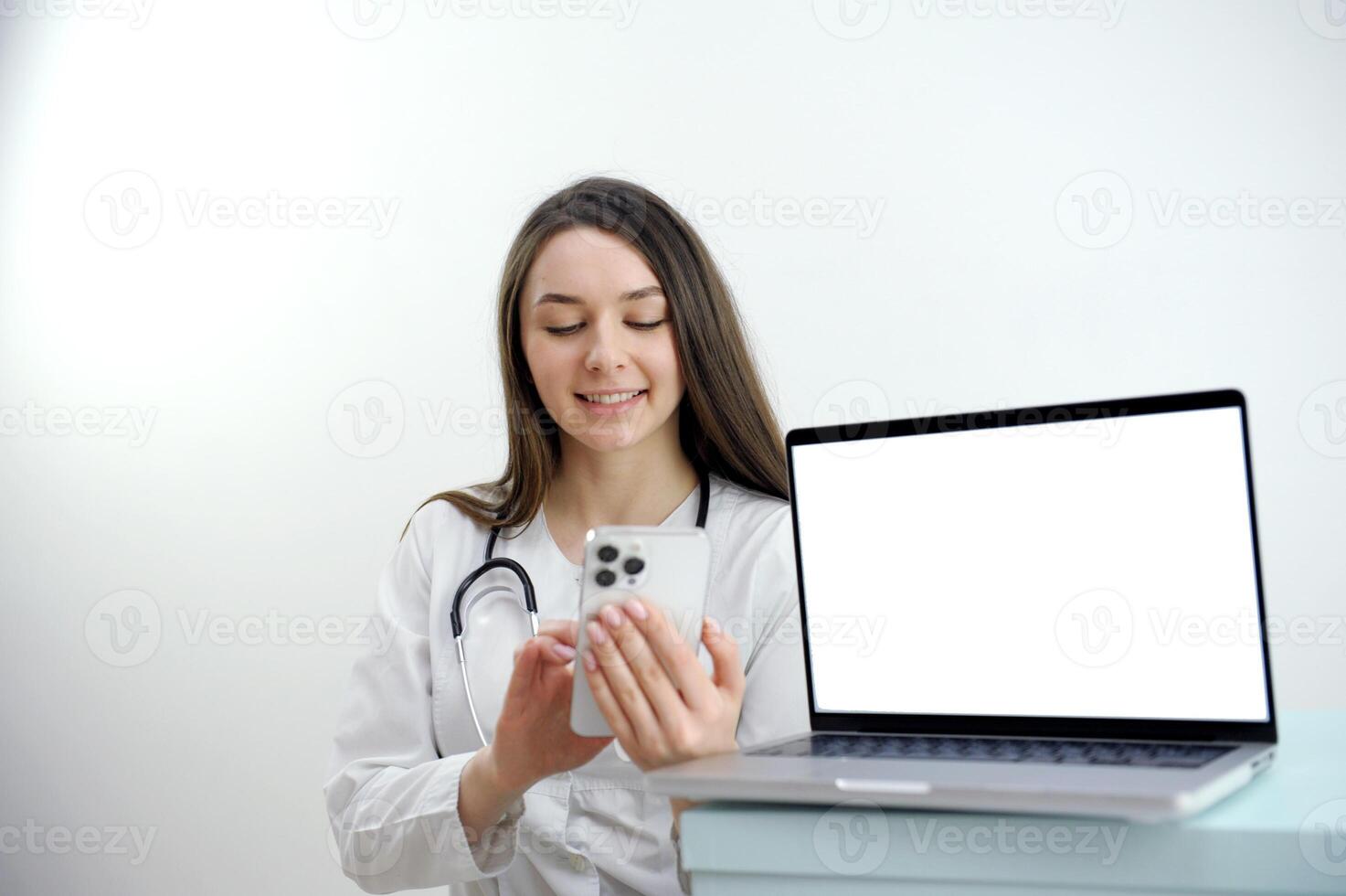 woman doctor working on the phone answering the call in front of her laptop with white screen space for advertising friendly female doctor over white background with a laptop photo